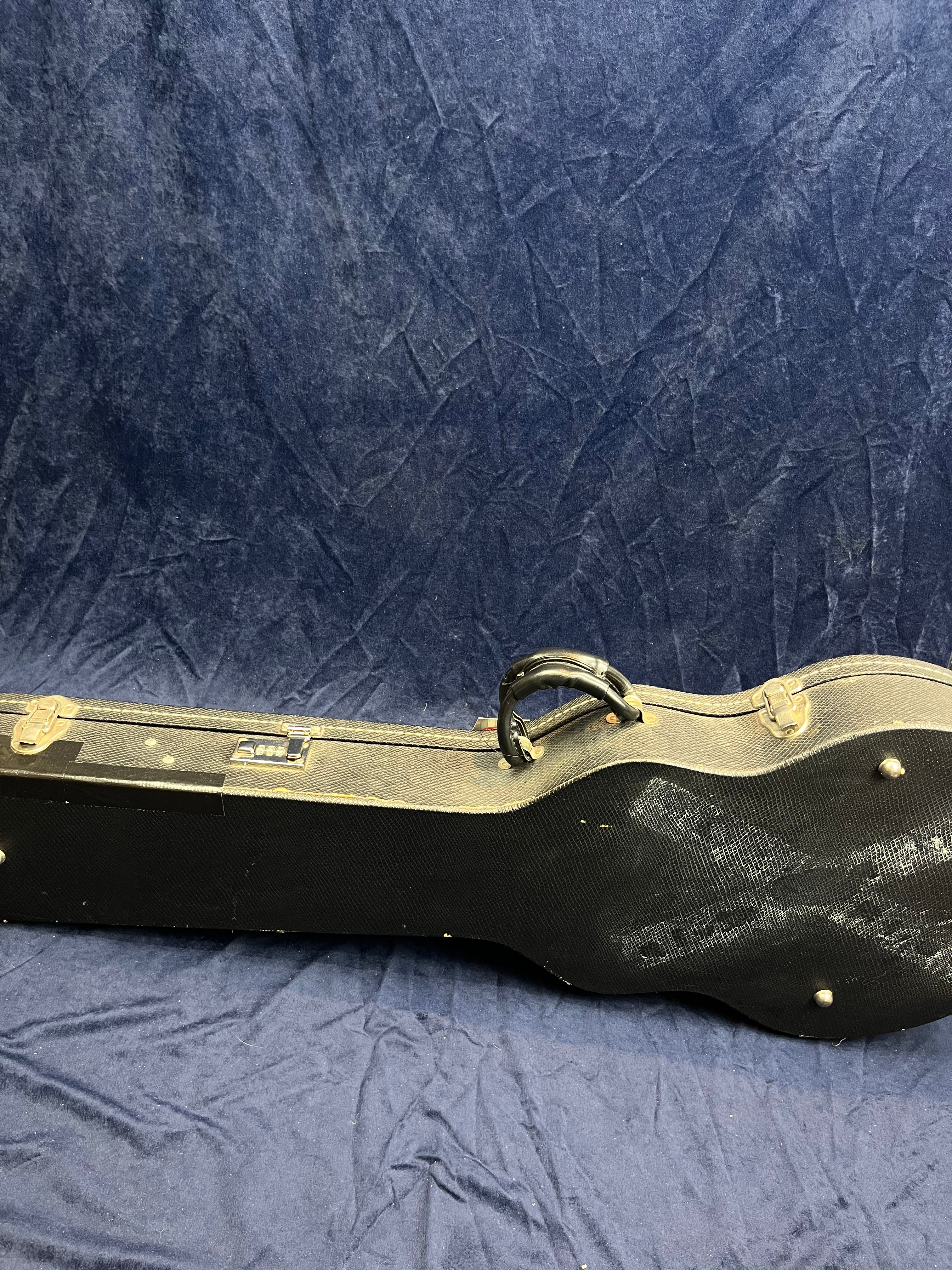Hard-shell black electric guitar case with metal clasps and a handle, resting on a blue textured fabric background.