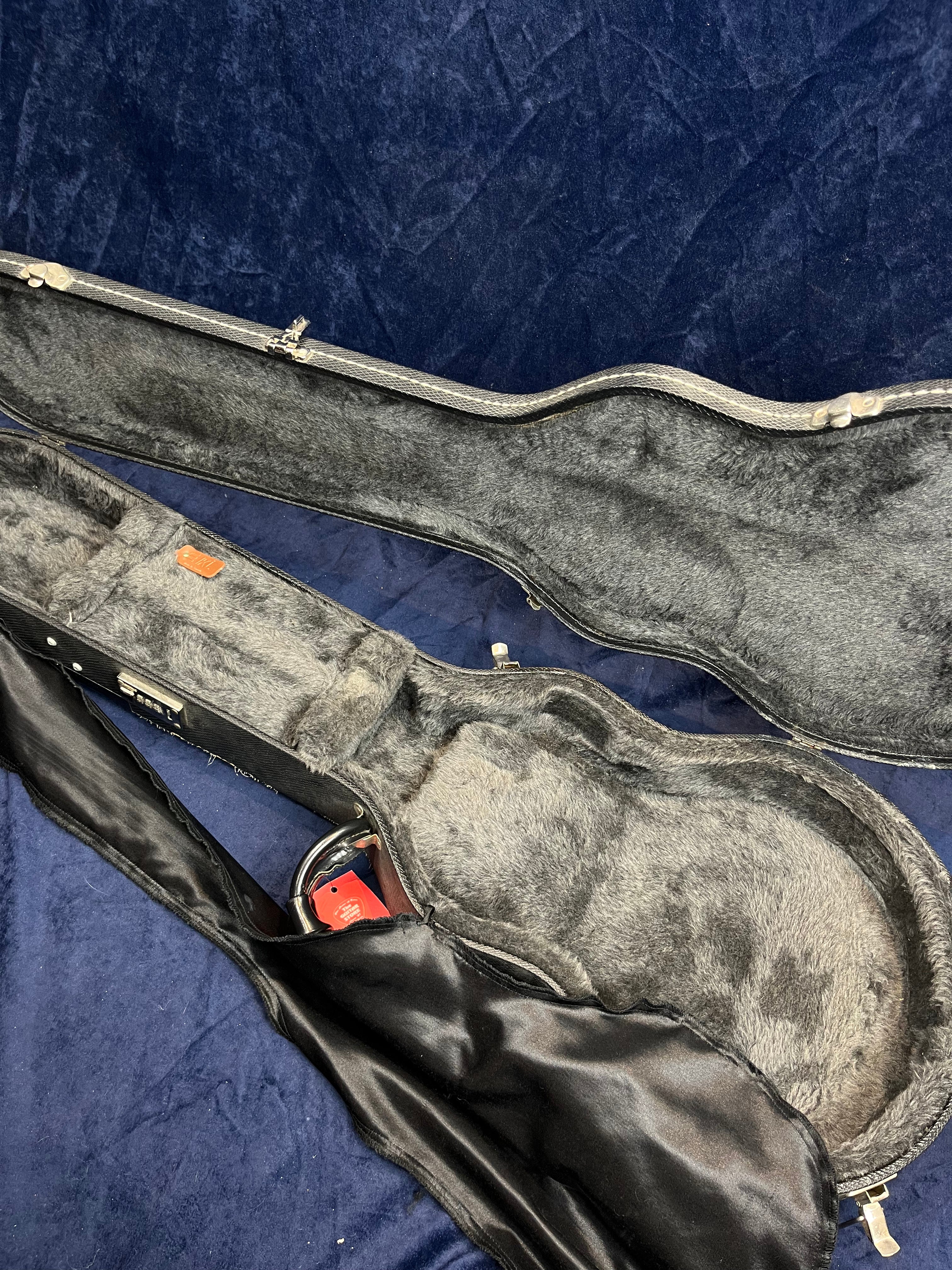 Empty hard electric guitar case with plush gray lining, partially open, showing a black cloth cover and a red combination padlock inside.
