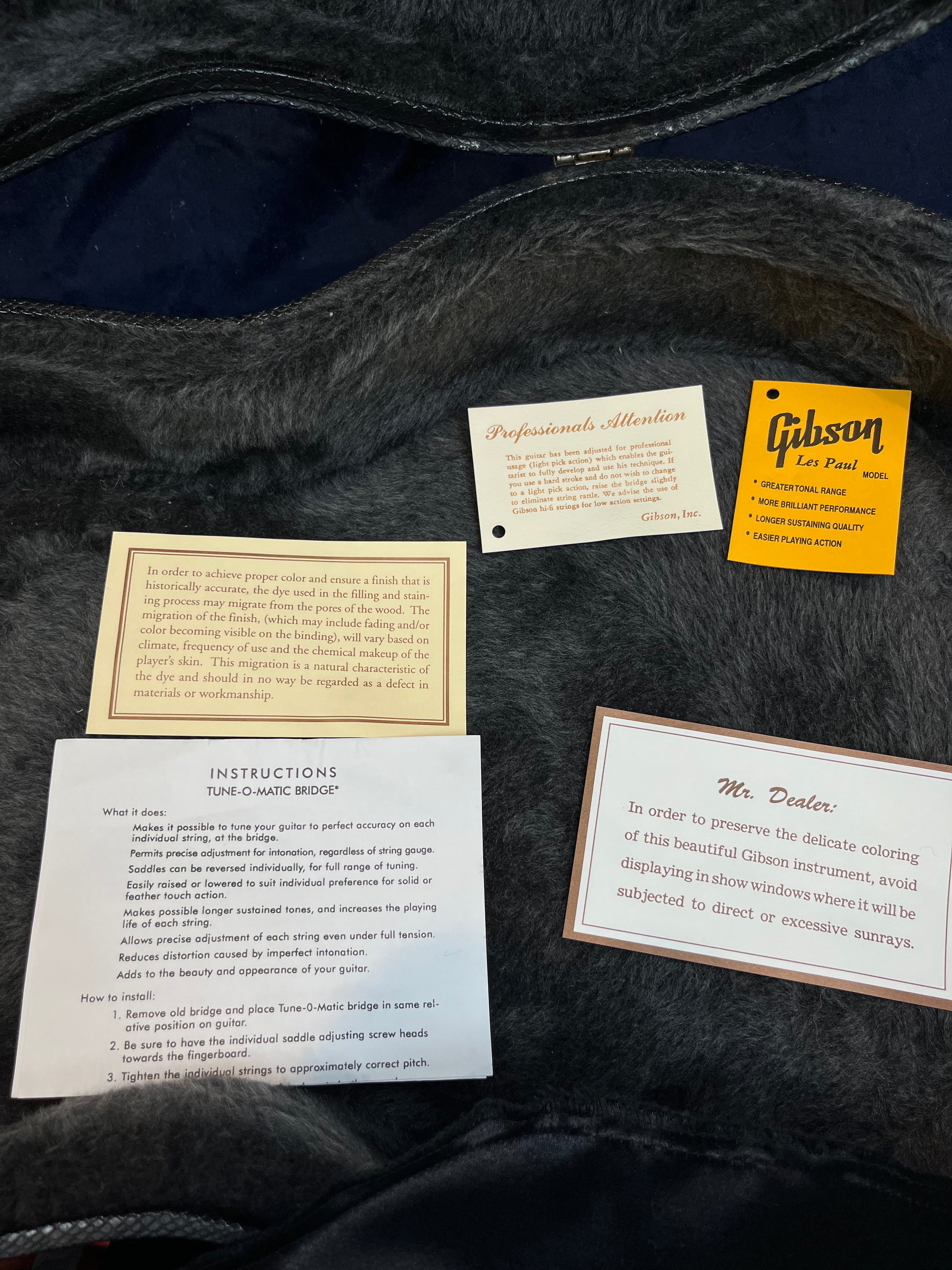 Five cards in a Gibson Les Paul electric guitar case give care instructions, tuning guide, and warnings about sunlight and dye migration affecting the finish.