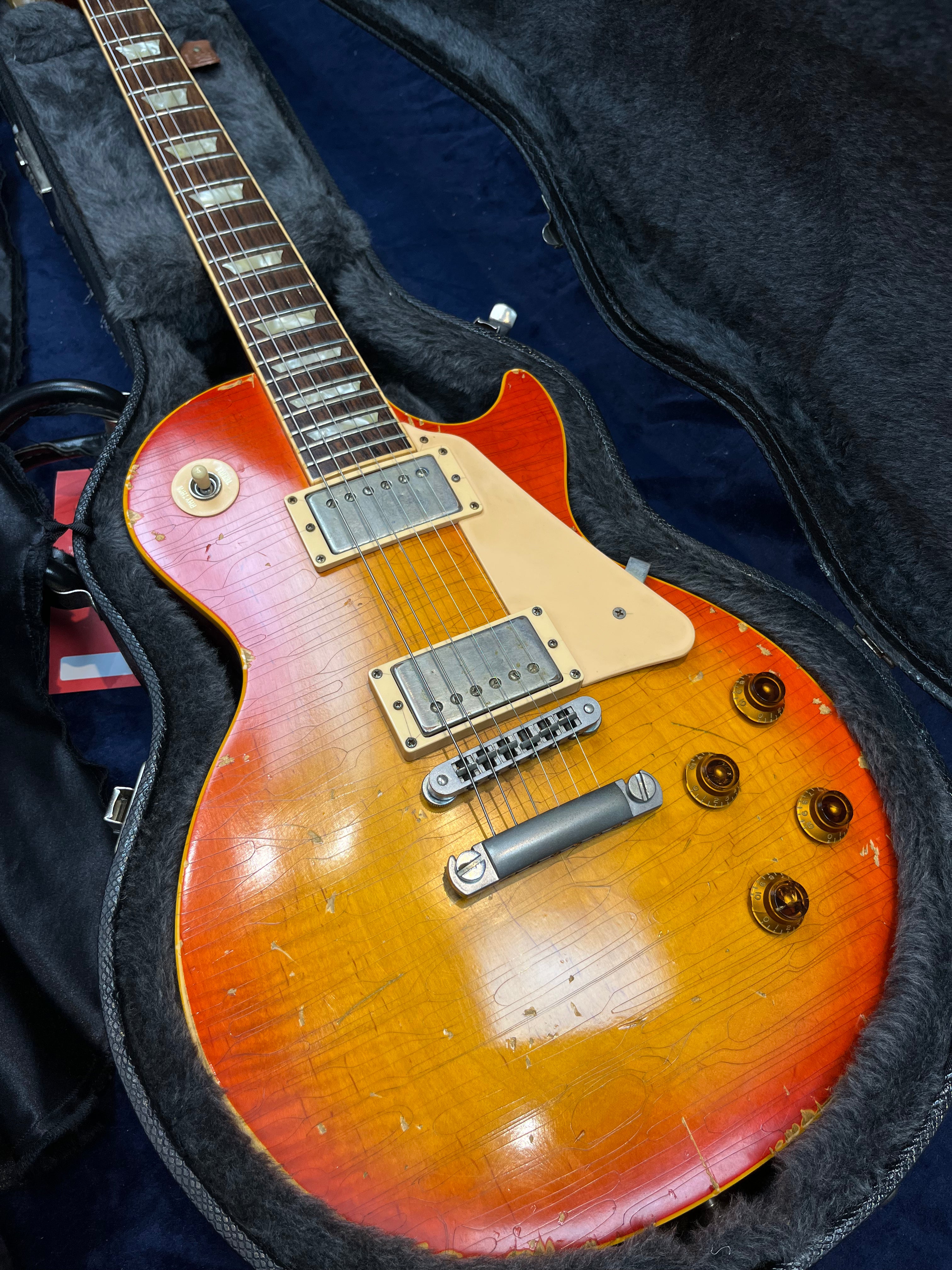 Sunburst finish electric guitar with aging marks, two humbucker pickups, four control knobs, and cream pickguard, resting in a black fur-lined case.