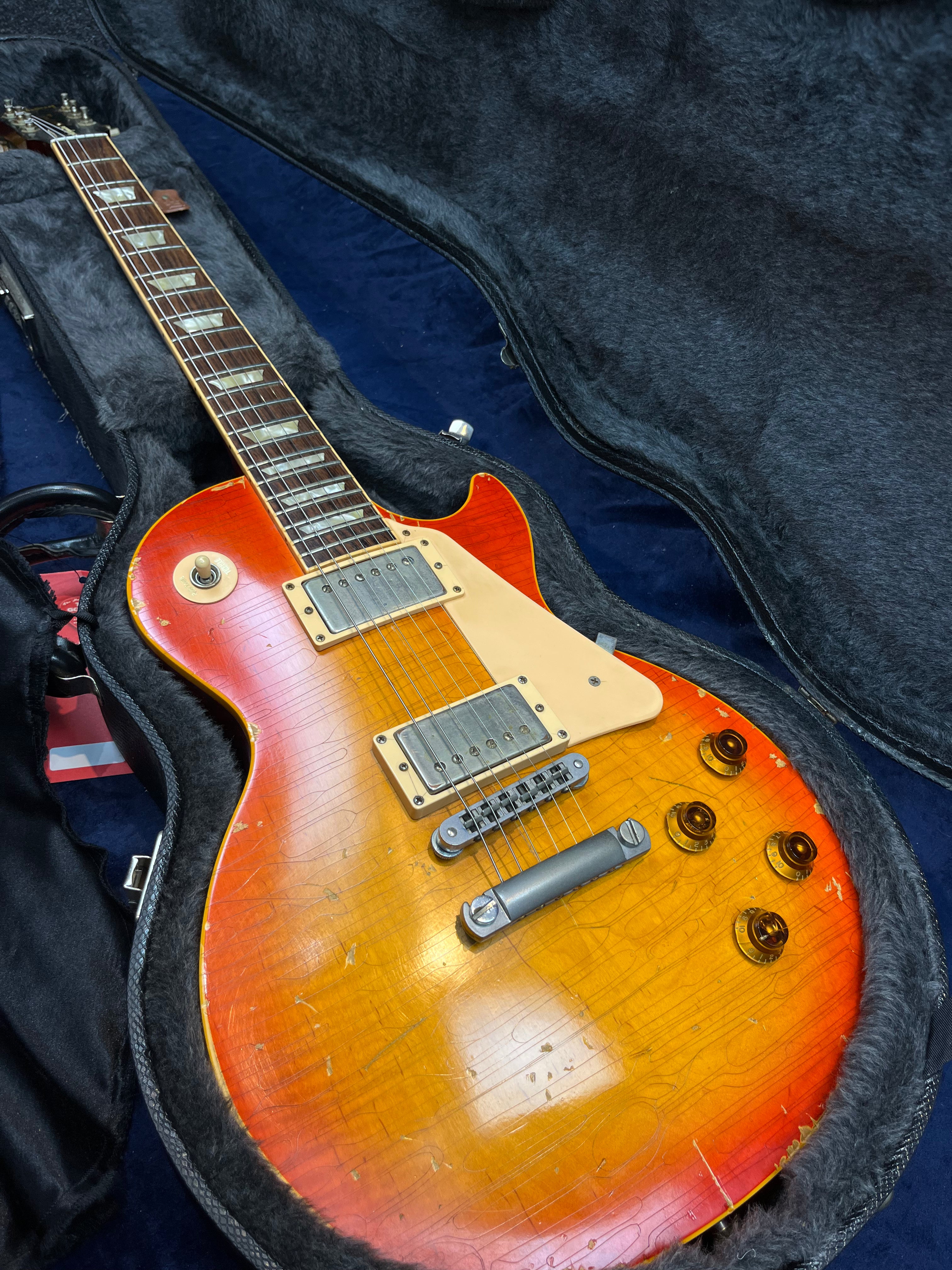 Sunburst electric guitar with a single cutaway, two humbucker pickups, gold knobs, and visible wear, resting in a lined hardshell case.