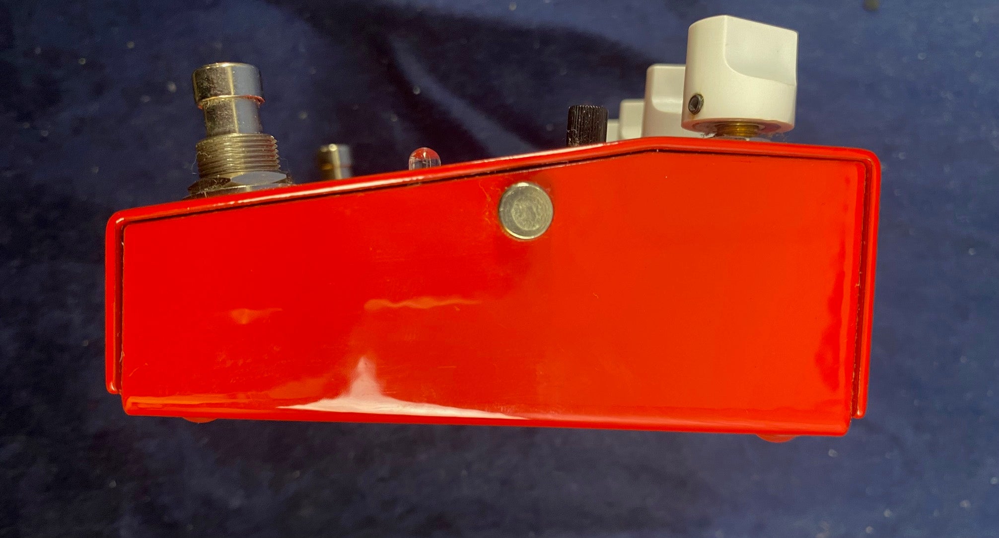 Red FX pedal with a metallic footswitch, two white control knobs, a black knob, and an LED indicator on a dark surface.