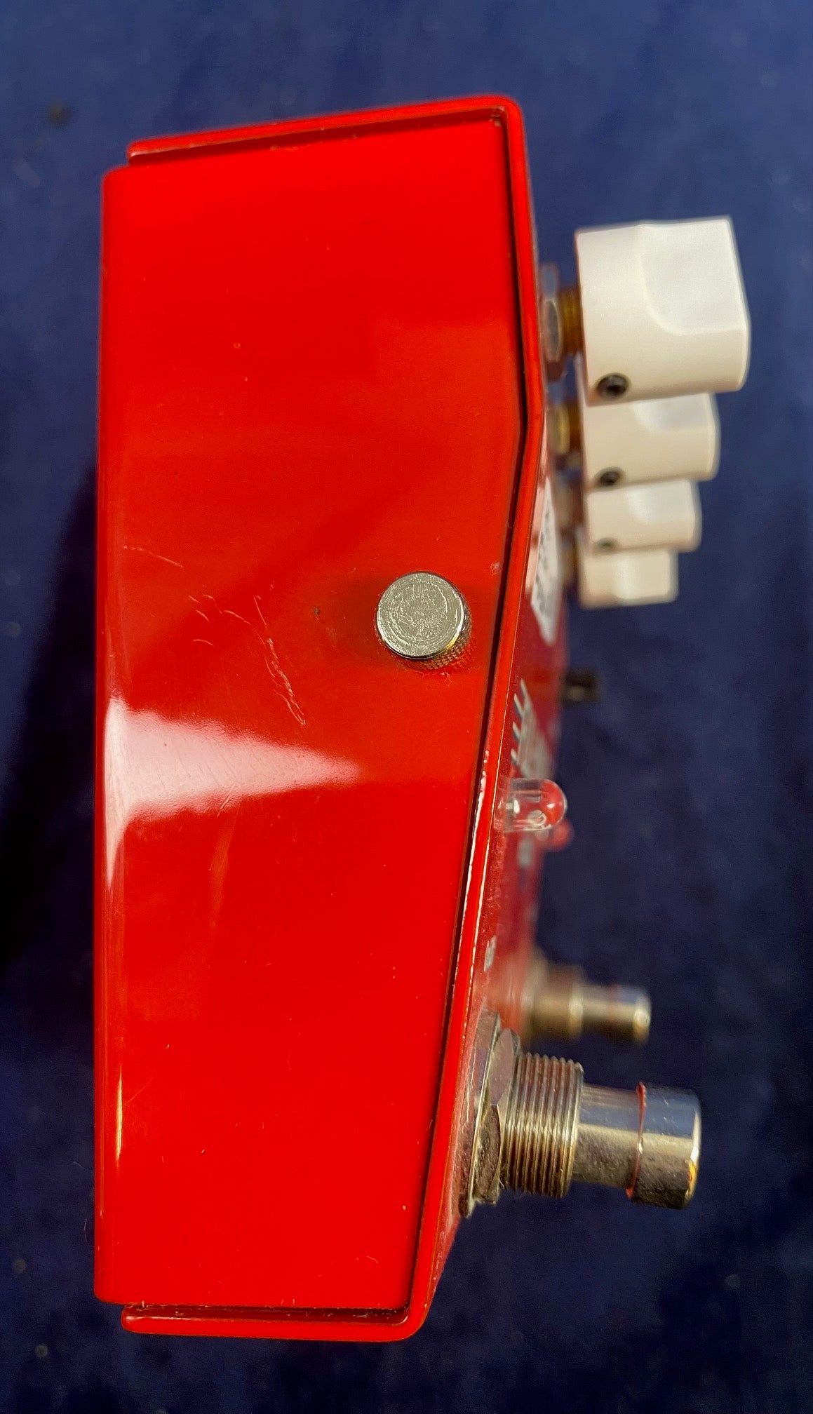 Red FX pedal with visible metal footswitches, white control knobs, and a small metal screw on the side. The surface has light scratches.