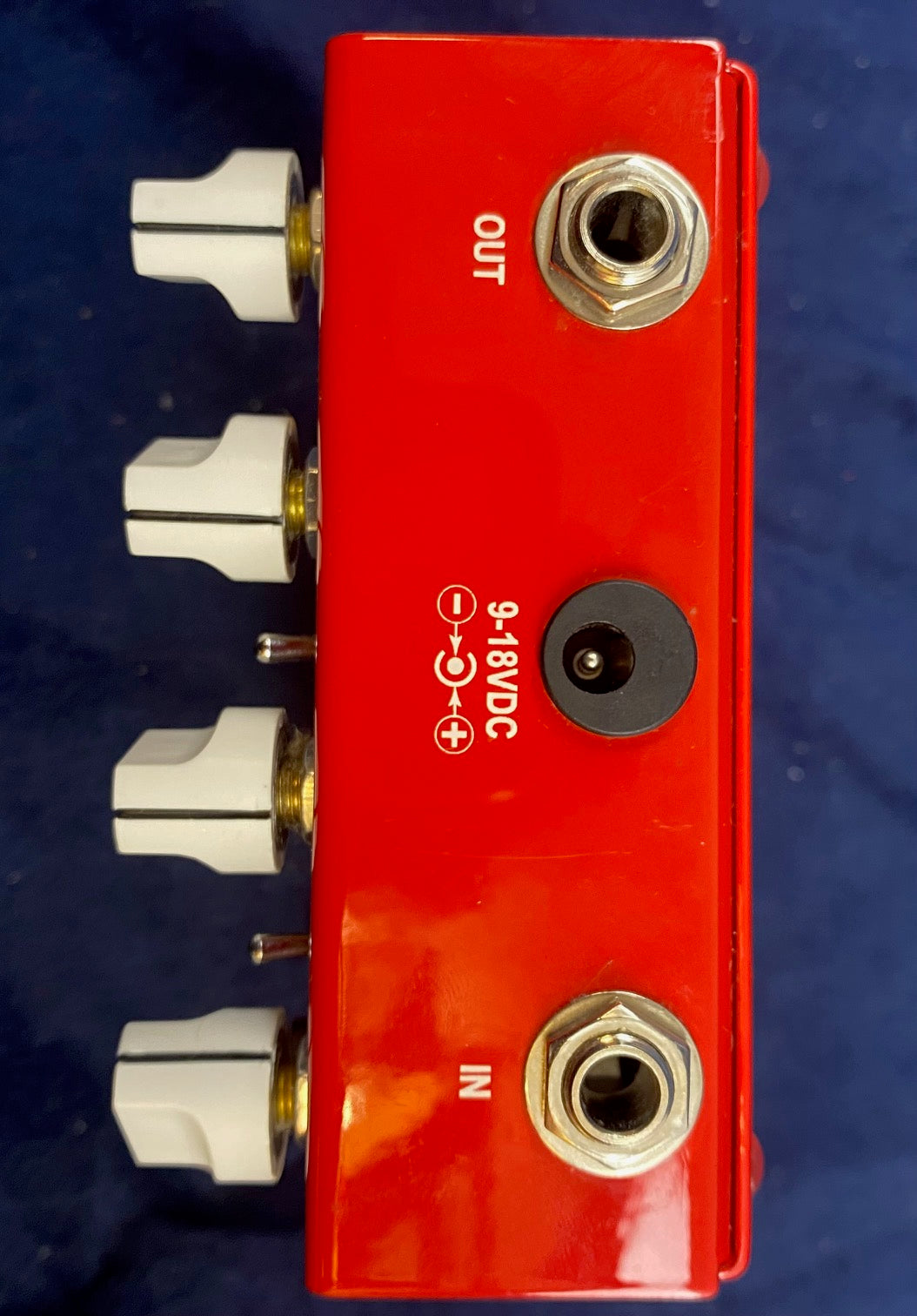 Red FX pedal with white knobs on the side, IN and OUT quarter-inch jacks, and a 9-18V DC power input on the top panel.