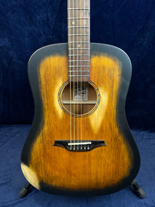Acoustic guitar with a sunburst finish, dark edges, six strings, round soundhole with decorative ring, and a uniquely shaped dark wood bridge.
