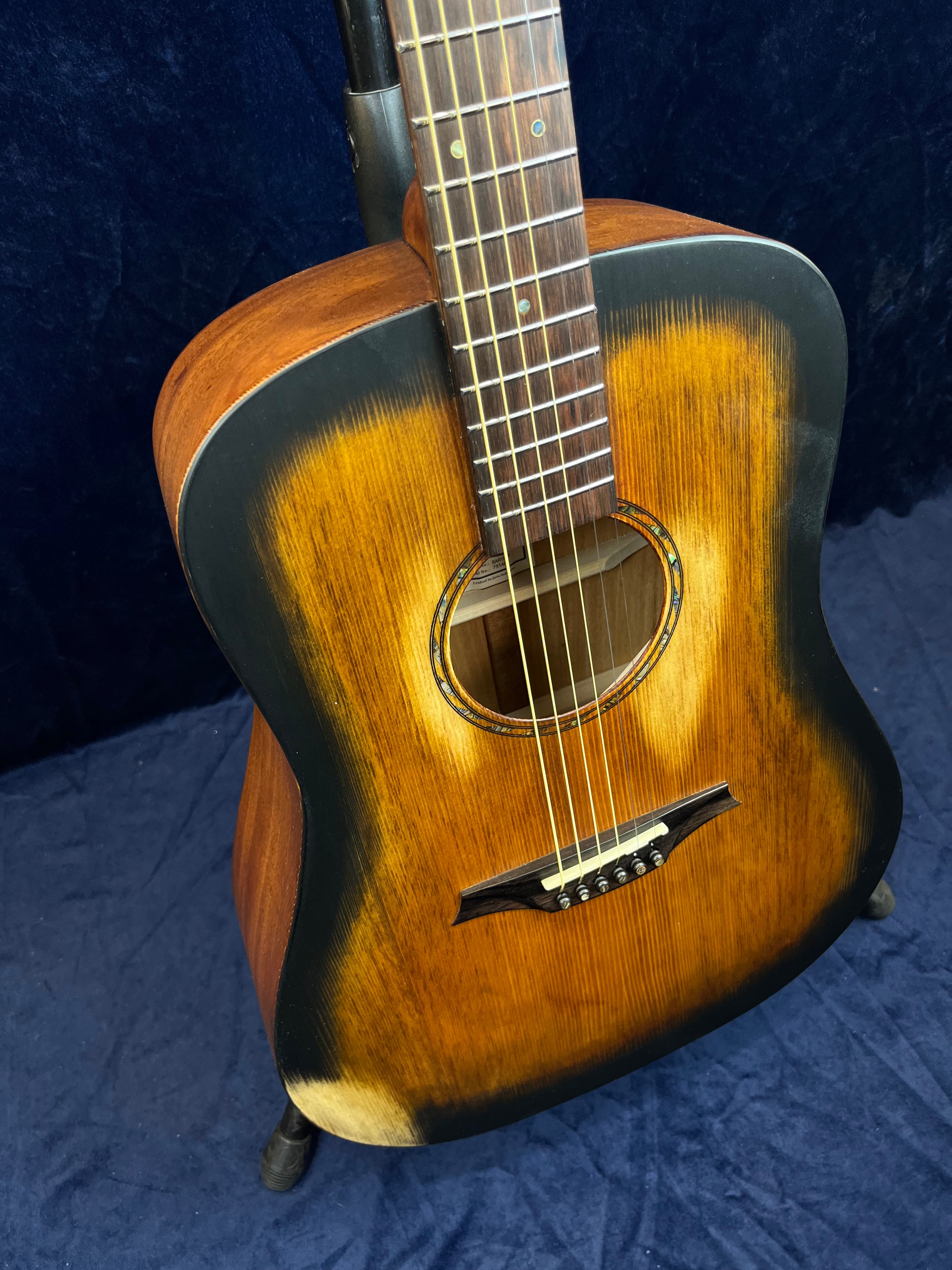 Acoustic guitar with a sunburst finish, dark edges fading into a golden brown center, six strings, and a scalloped-style bridge.