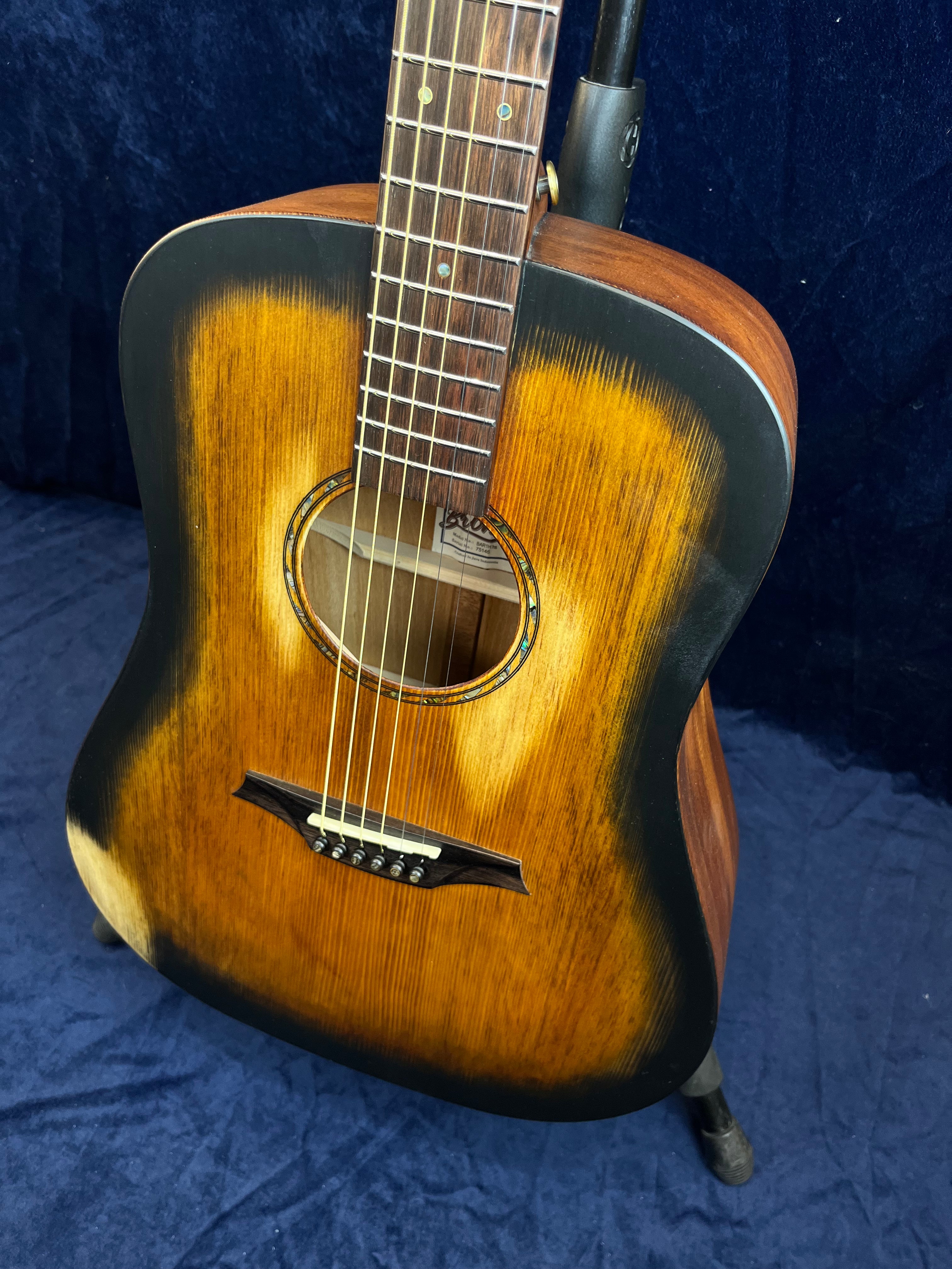 Acoustic guitar with a sunburst finish, dark edges, a round sound hole, six strings, wooden bridge, and visible wood grain on the body.