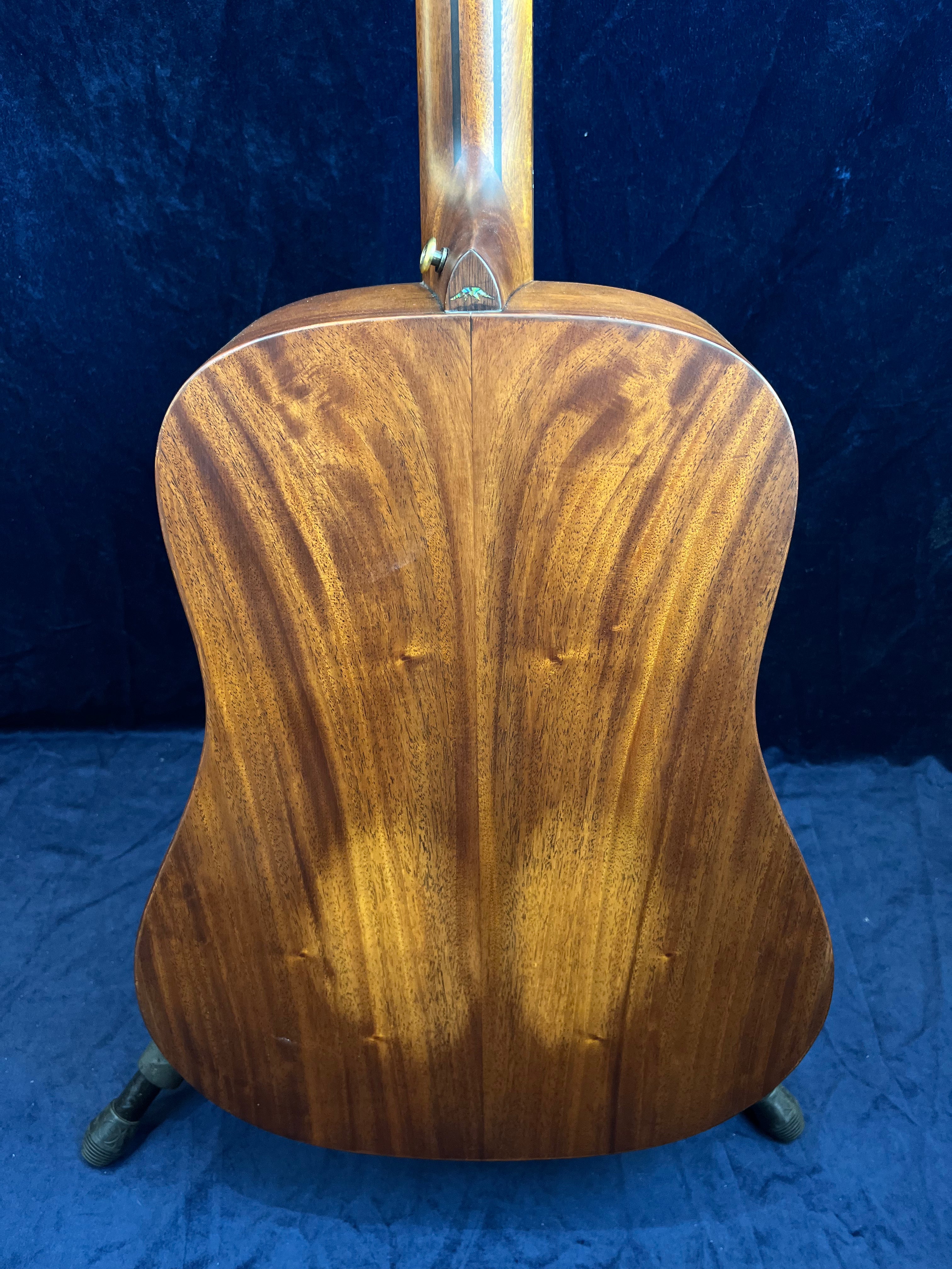 Back view of an acoustic guitar showing rich, warm brown wood with a pronounced natural grain and a seam down the center.