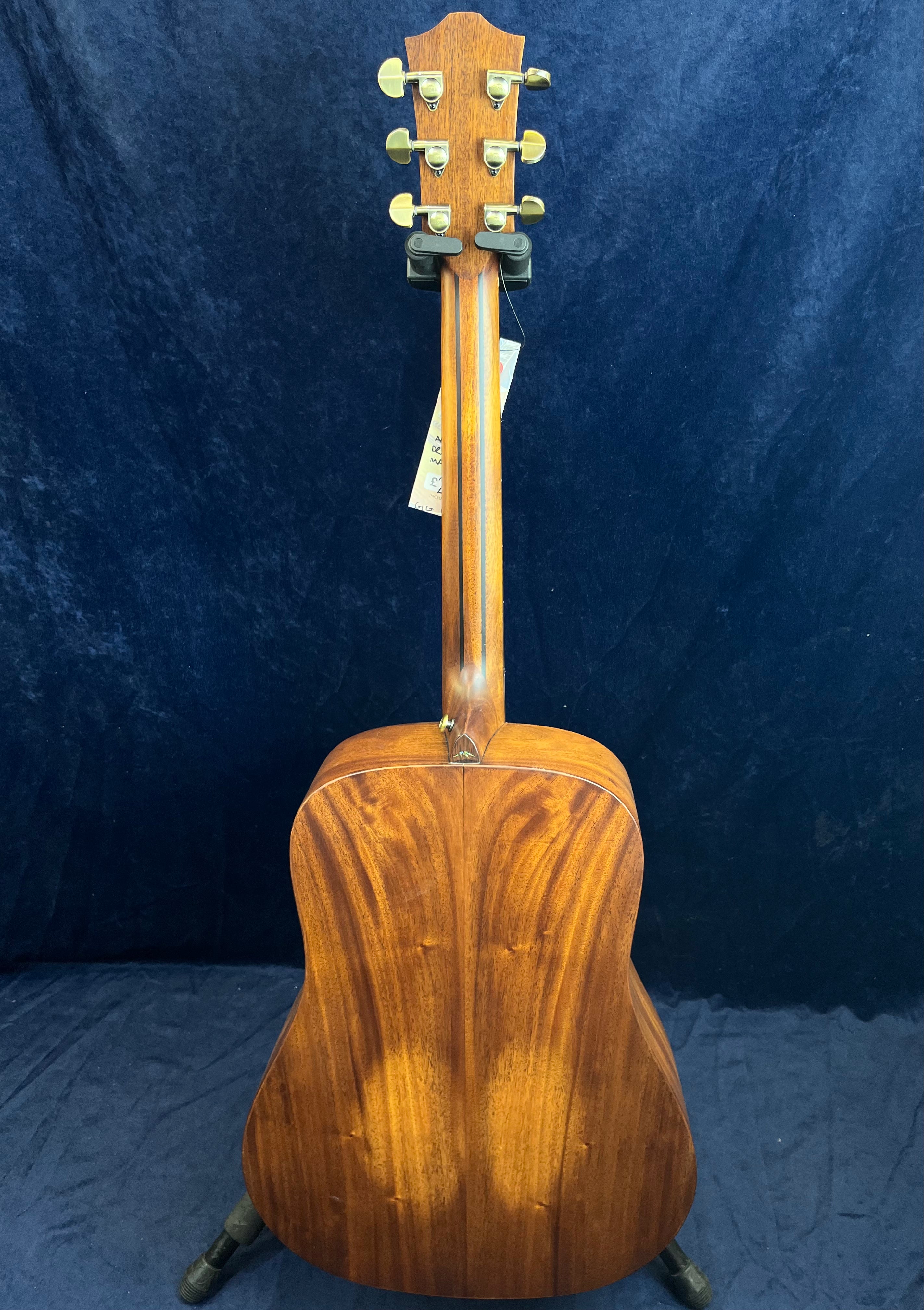 Rear view of an acoustic guitar with a rich brown wood finish, gold tuning pegs, and a visible wood grain pattern on the back.