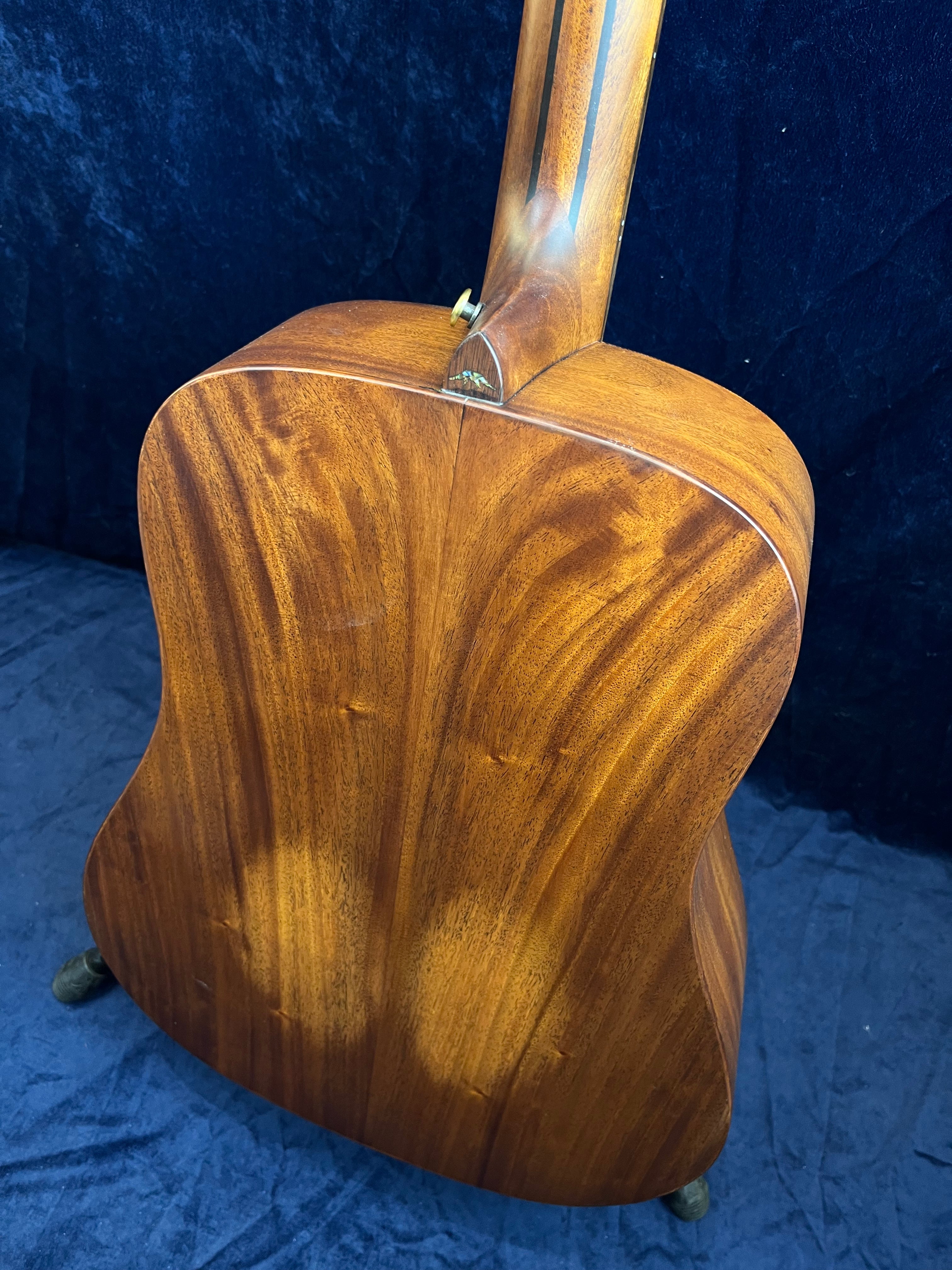 Back view of an acoustic guitar showing polished wood grain with a warm brown finish and visible seam down the center.