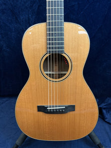 Light brown acoustic guitar with a glossy finish, black bridge, round sound hole, and a dark fretboard, displayed upright against a dark blue background.