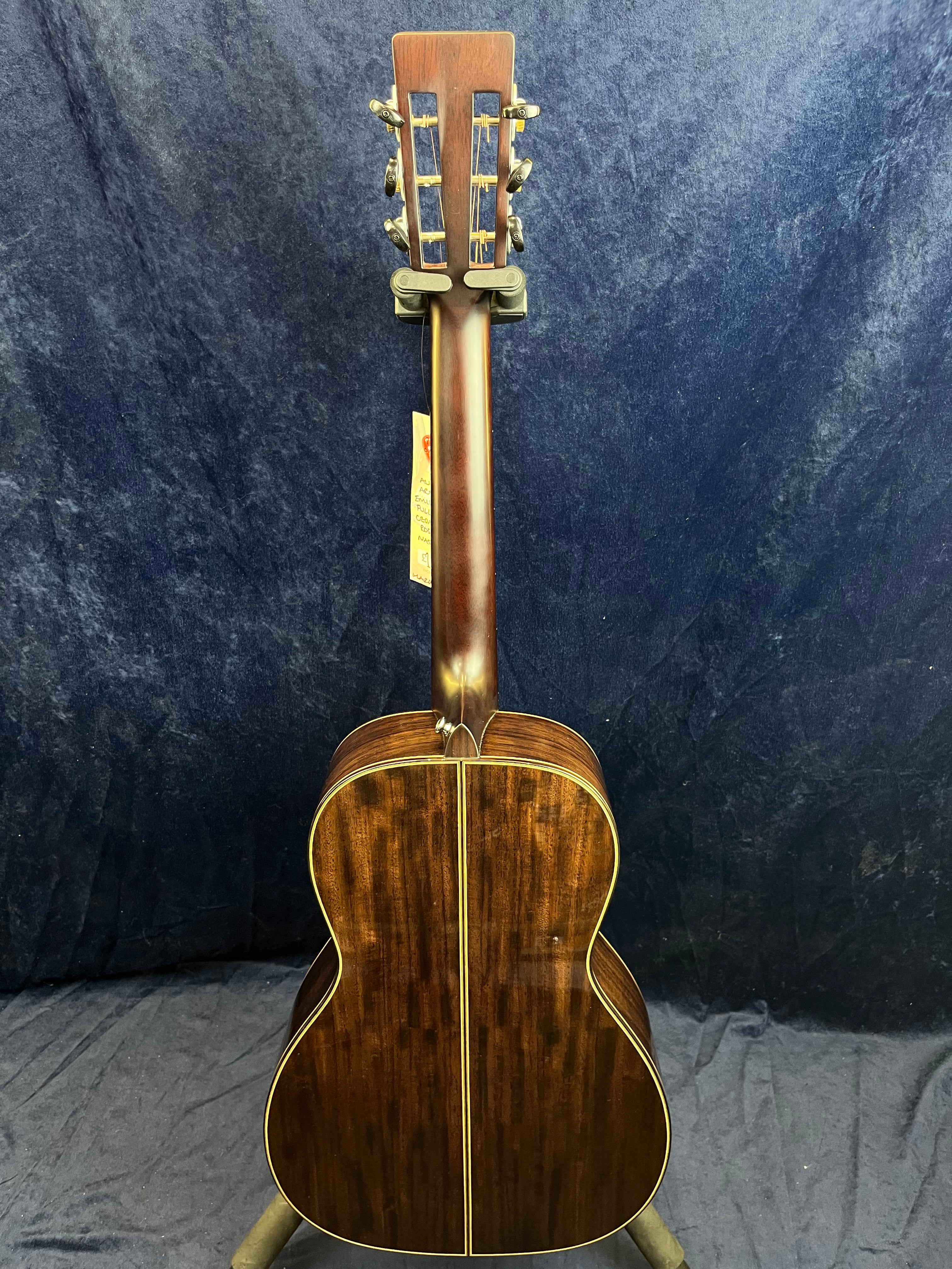 Acoustic guitar shown from the back with a dark, glossy wood finish, yellow binding along the edges, and a slotted headstock with metal tuning pegs.