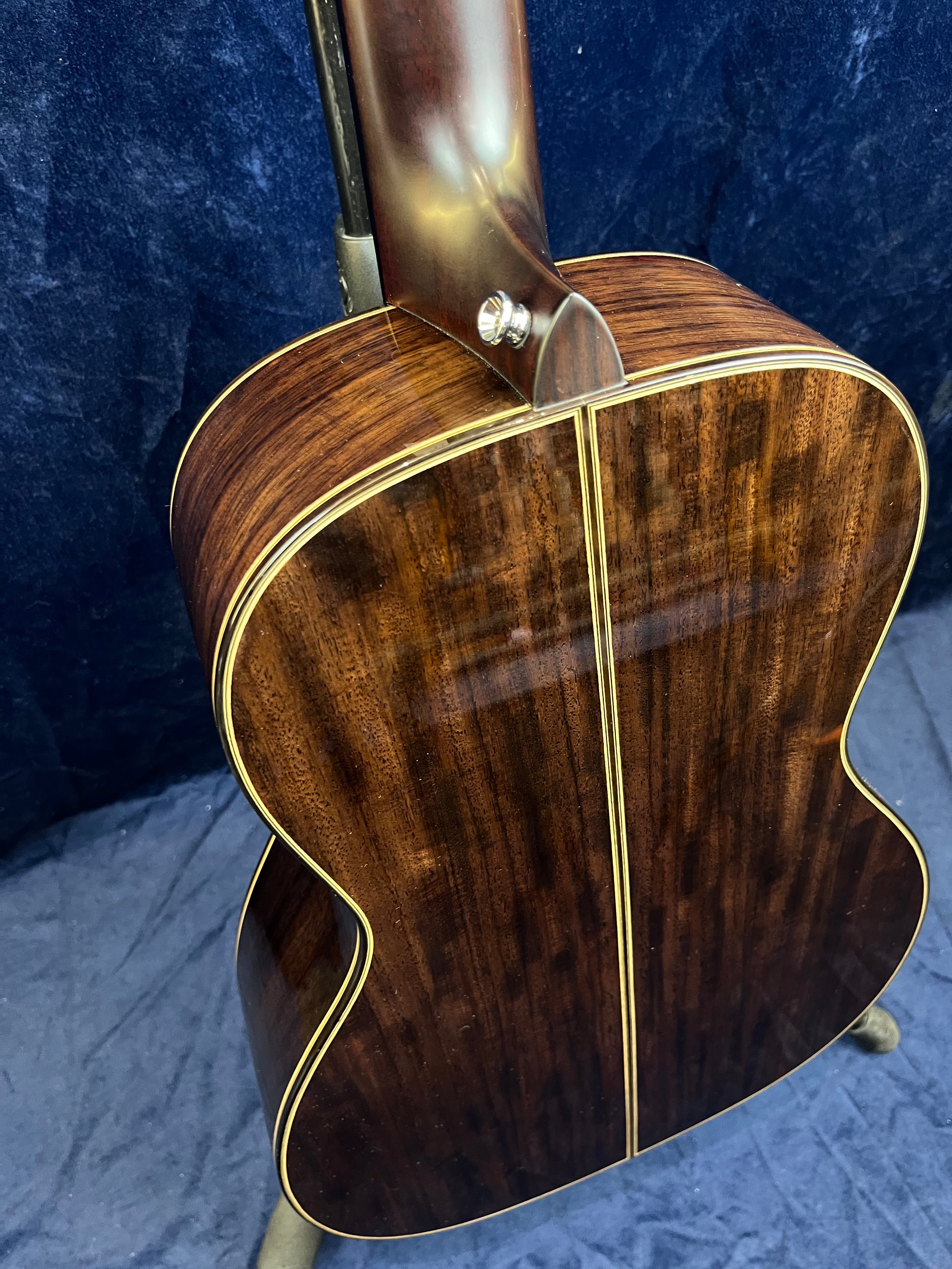 Dark, glossy wooden acoustic guitar back with a thin light center stripe and cream-colored edge binding, shown from the neck joint area.