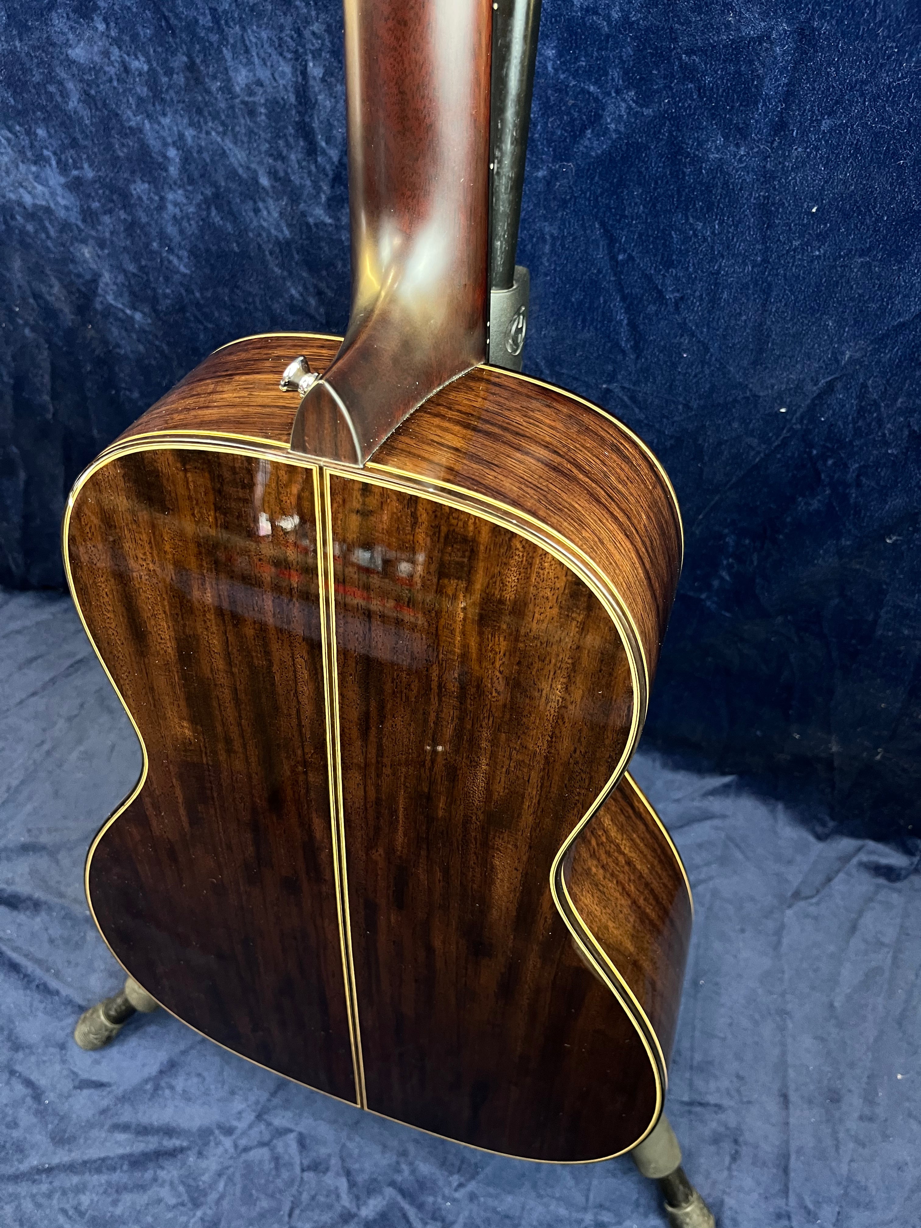 Acoustic guitar showing the glossy dark wood back with a central inlay stripe and light-colored binding along the edges.