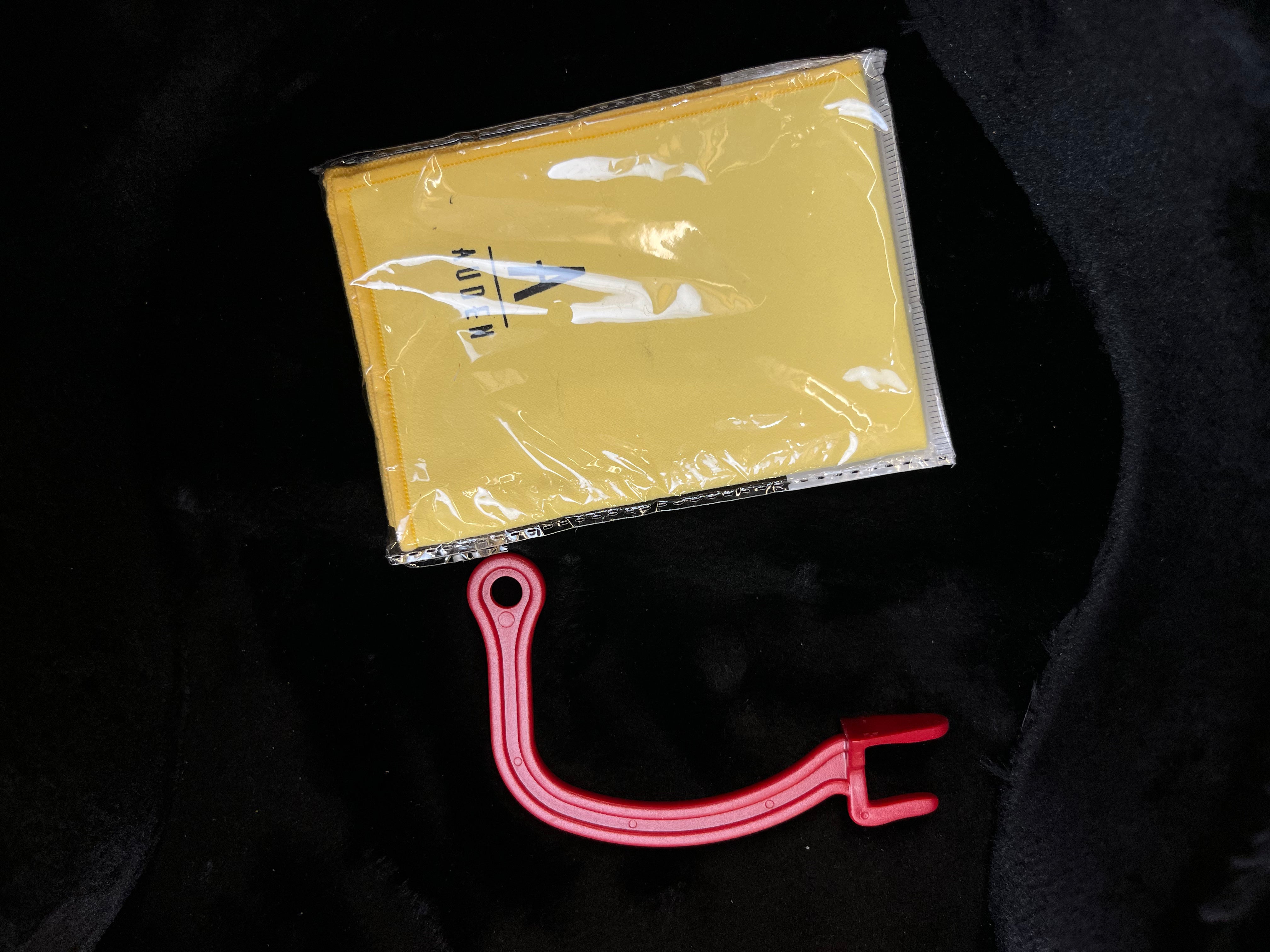 A yellow cleaning cloth in plastic packaging and a red string winder tool, both accessories for acoustic guitars, placed on a black surface.
