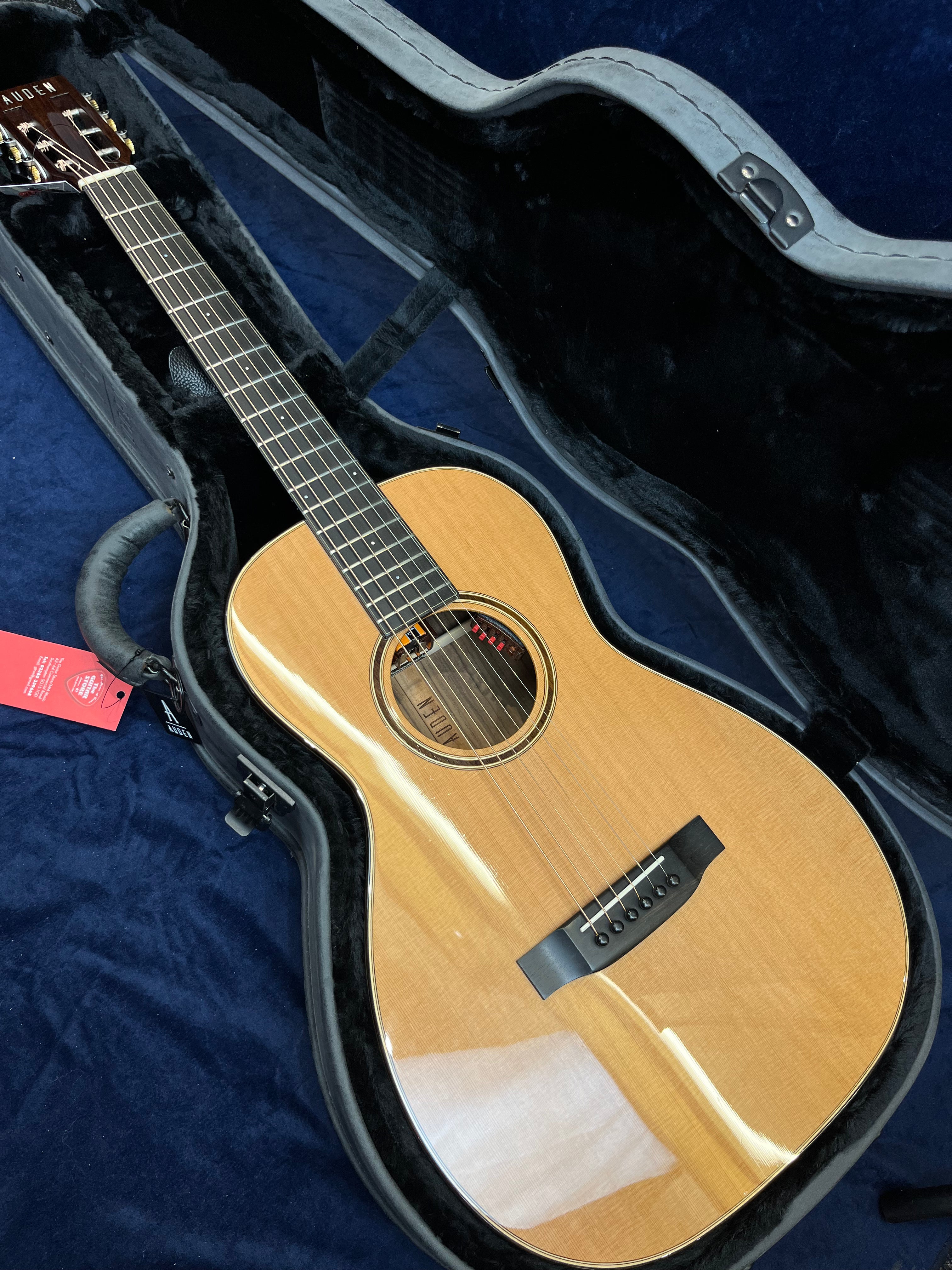 Small-bodied acoustic guitar with a glossy natural wood finish, six strings, and black bridge, resting inside a foam-lined hard case.