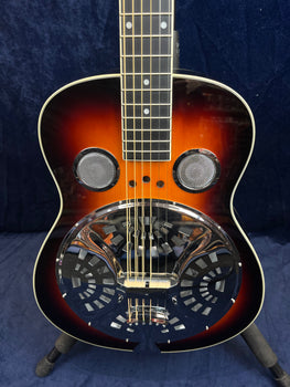 A resonator guitar with a sunburst finish, two circular sound holes, and a large chrome resonator coverplate with geometric cutouts on the body.