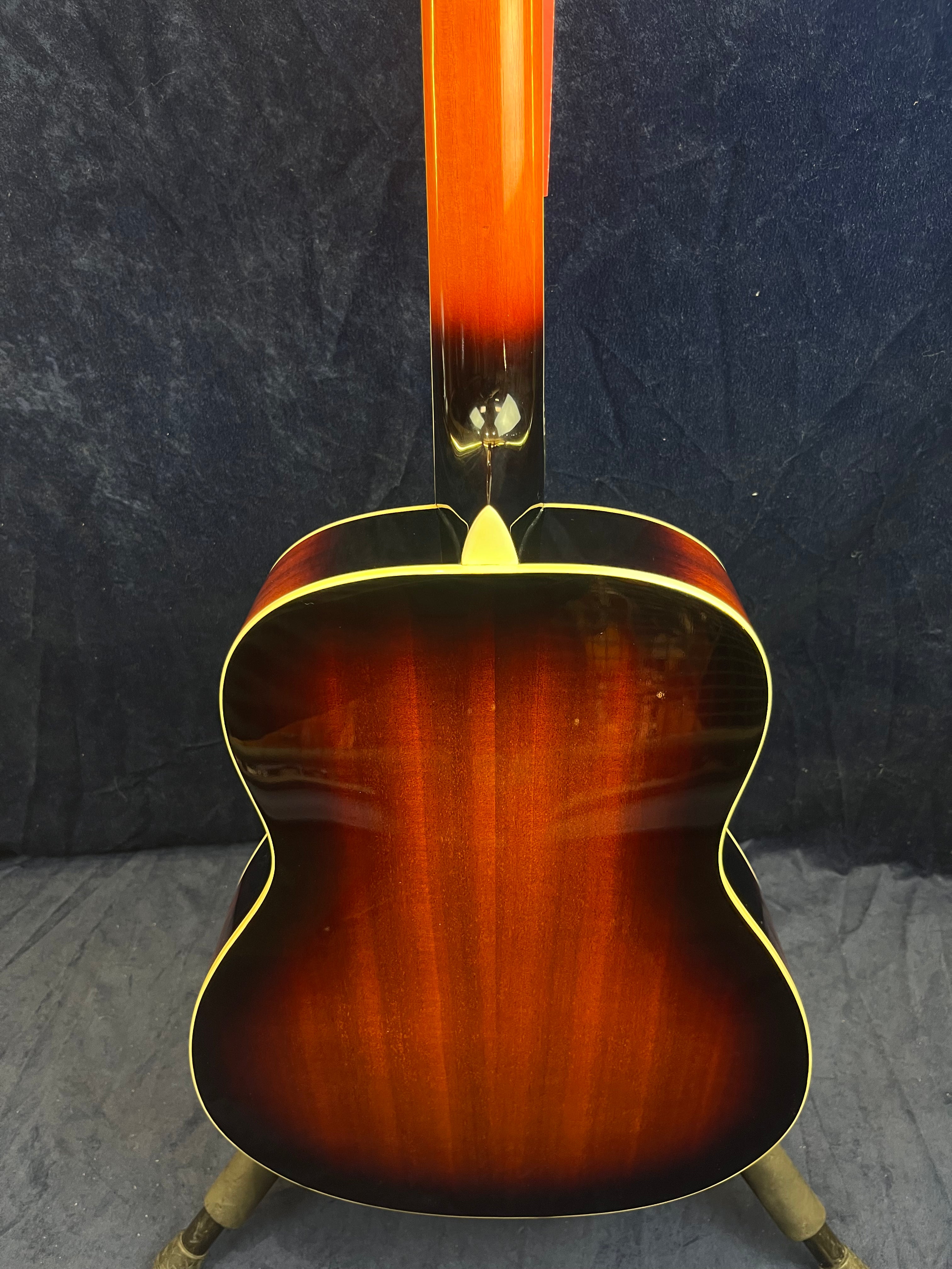 Warm sunburst finish resonator guitar seen from the back, with a glossy reddish-brown body, yellow binding, and a straight neck against a dark background.