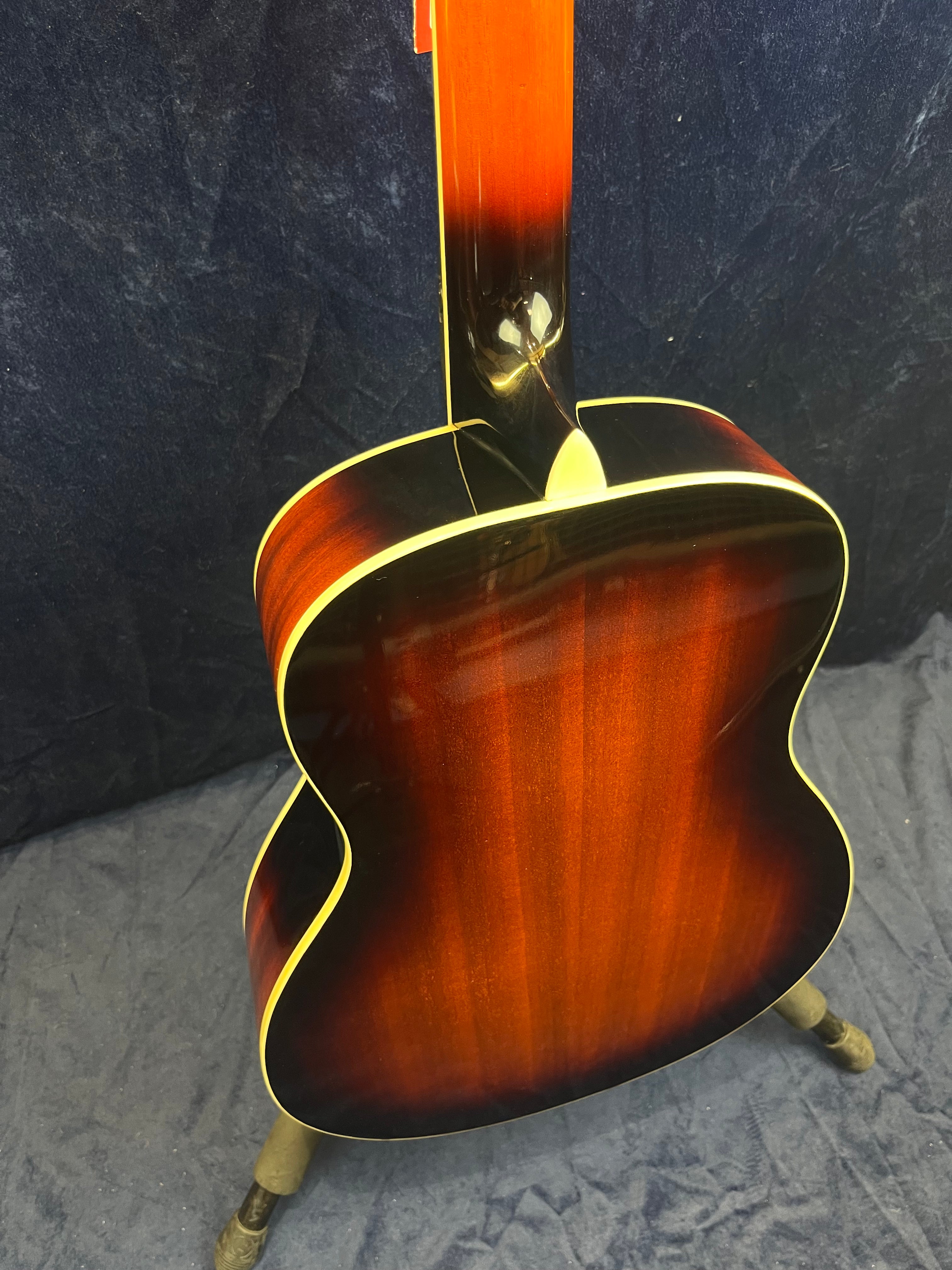 A resonator guitar on a stand, shown from the back with a glossy sunburst finish and cream binding along the edges.
