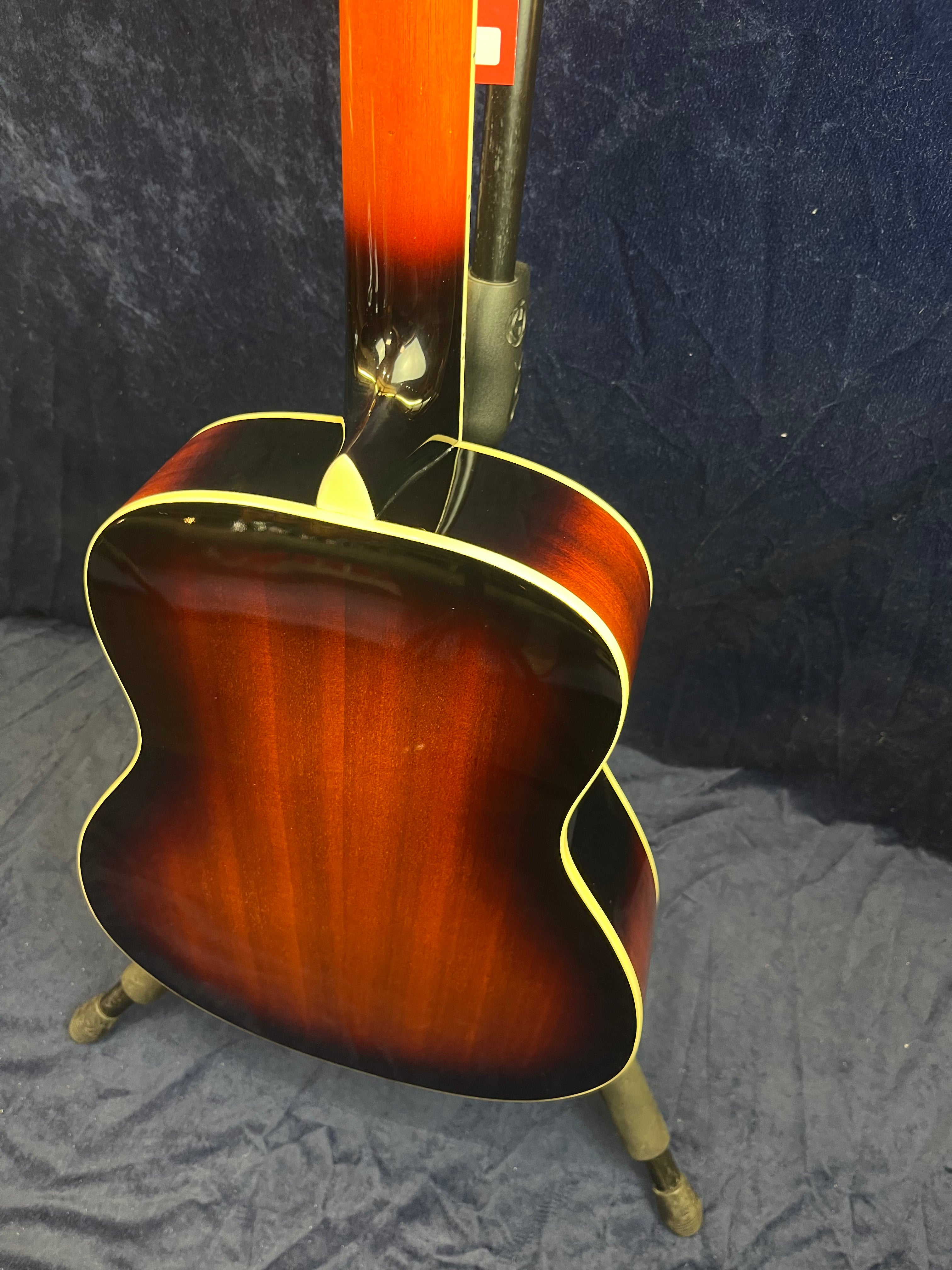 A resonator guitar showing its glossy, sunburst-finished back and neck with cream binding, resting on a stand against a dark background.