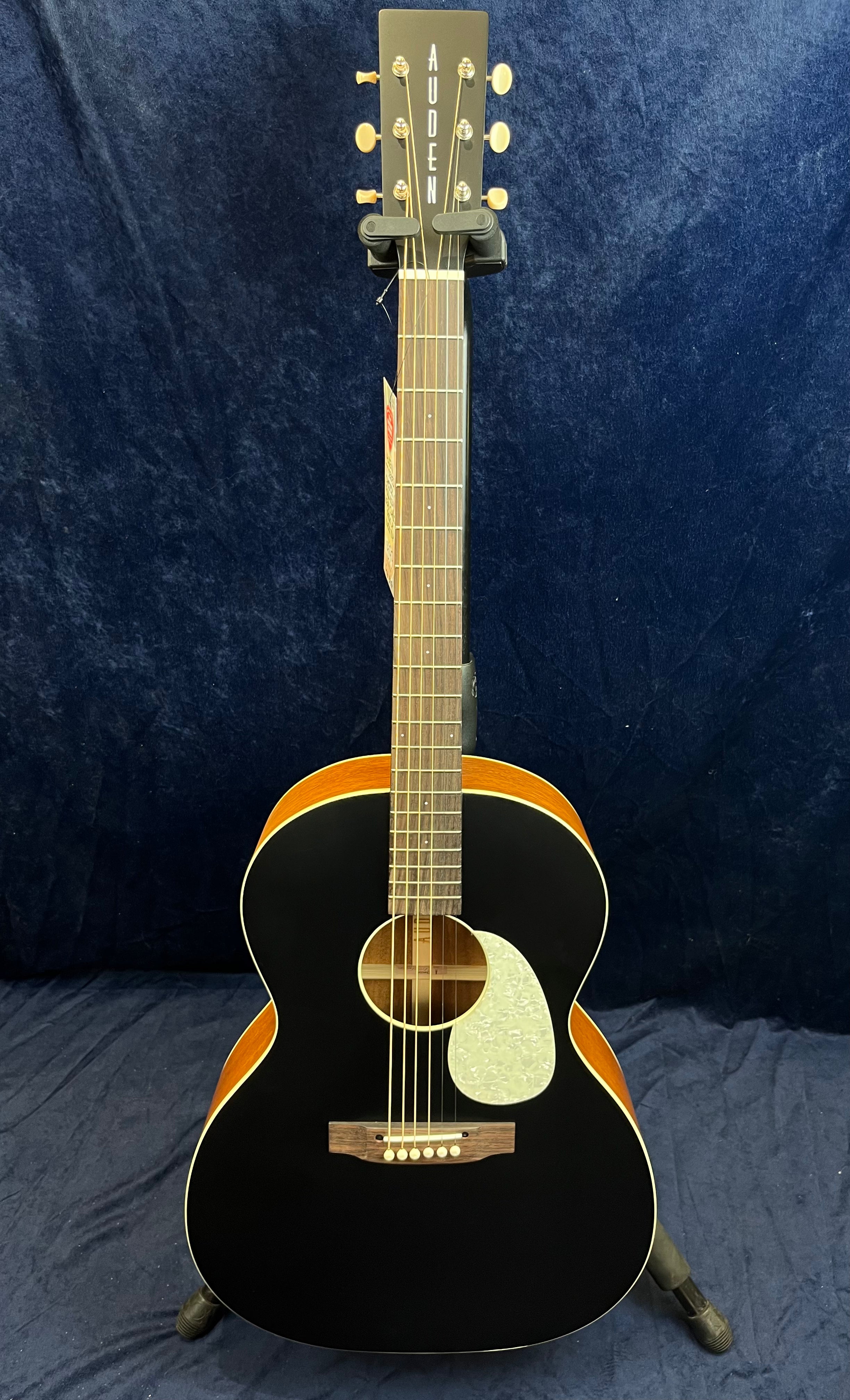 Guitare acoustique à table noire, éclisses et dos couleur bois, pickguard blanc nacré, six cordes, tête marquée « AUDEN » en lettres blanches.