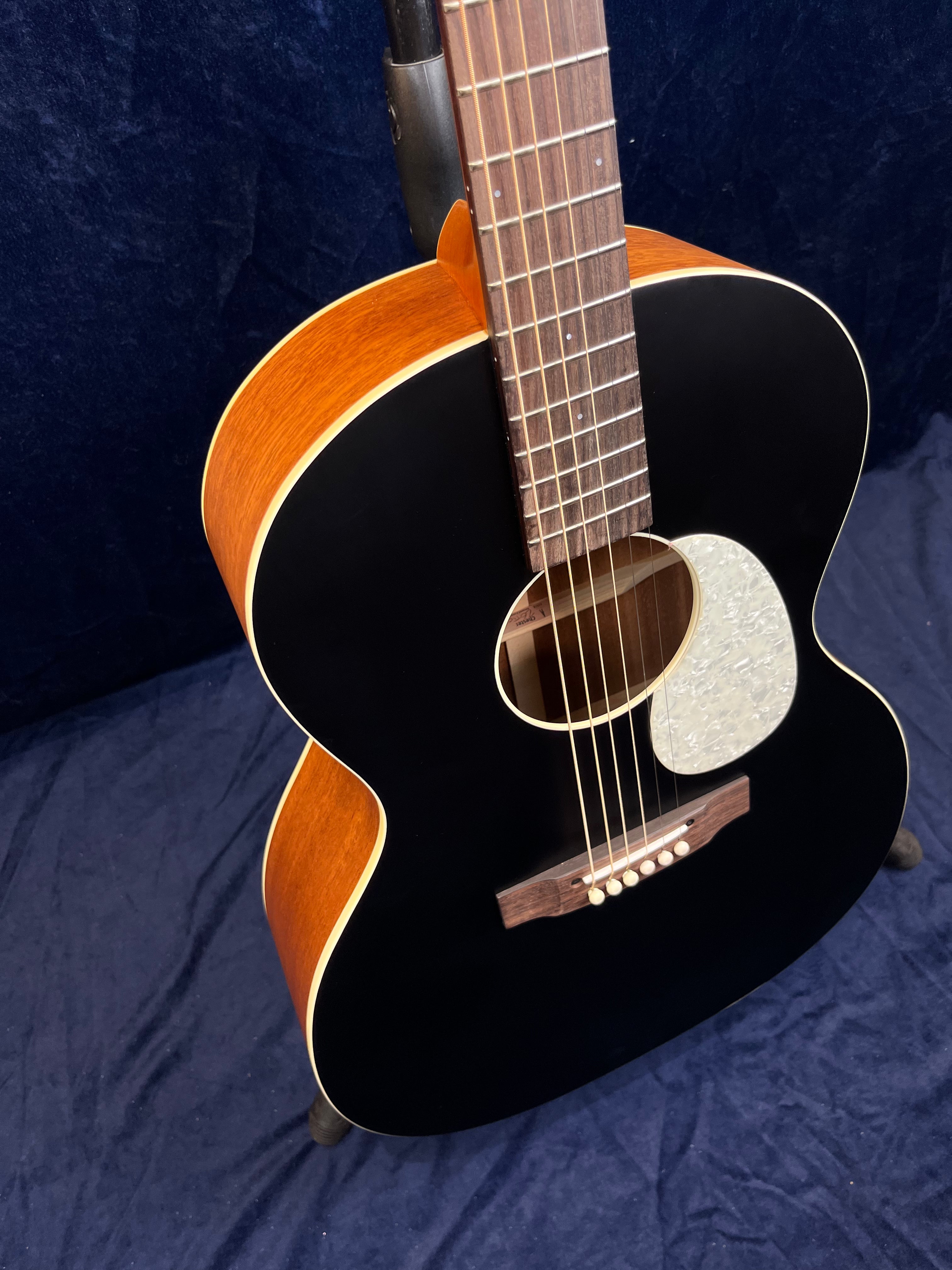 Guitare acoustique avec table noire, éclisses et dos couleur bois, pickguard nacré et chevalet en bois foncé, posée sur un fond bleu foncé.
