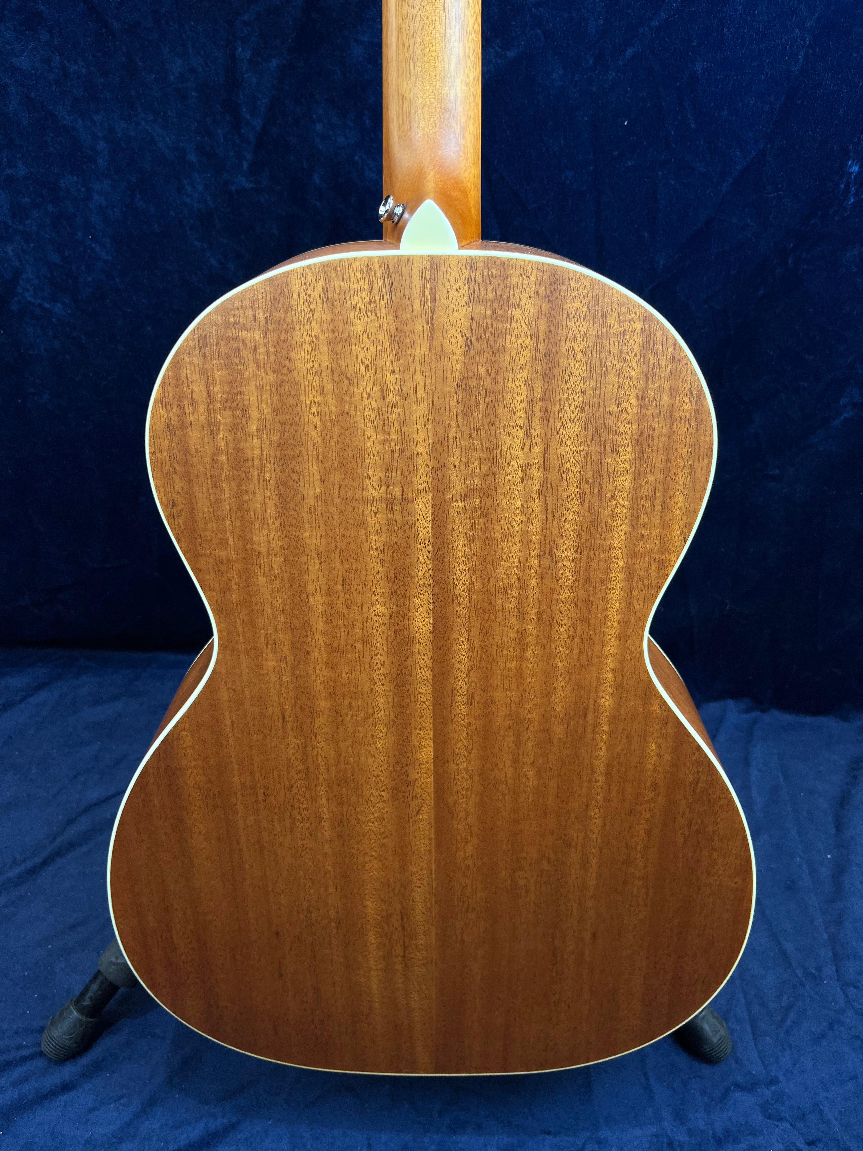 Fond d’une guitare acoustique en bois brun à grain droit, contours arrondis avec filet clair, manche visible en haut, posée sur support noir.