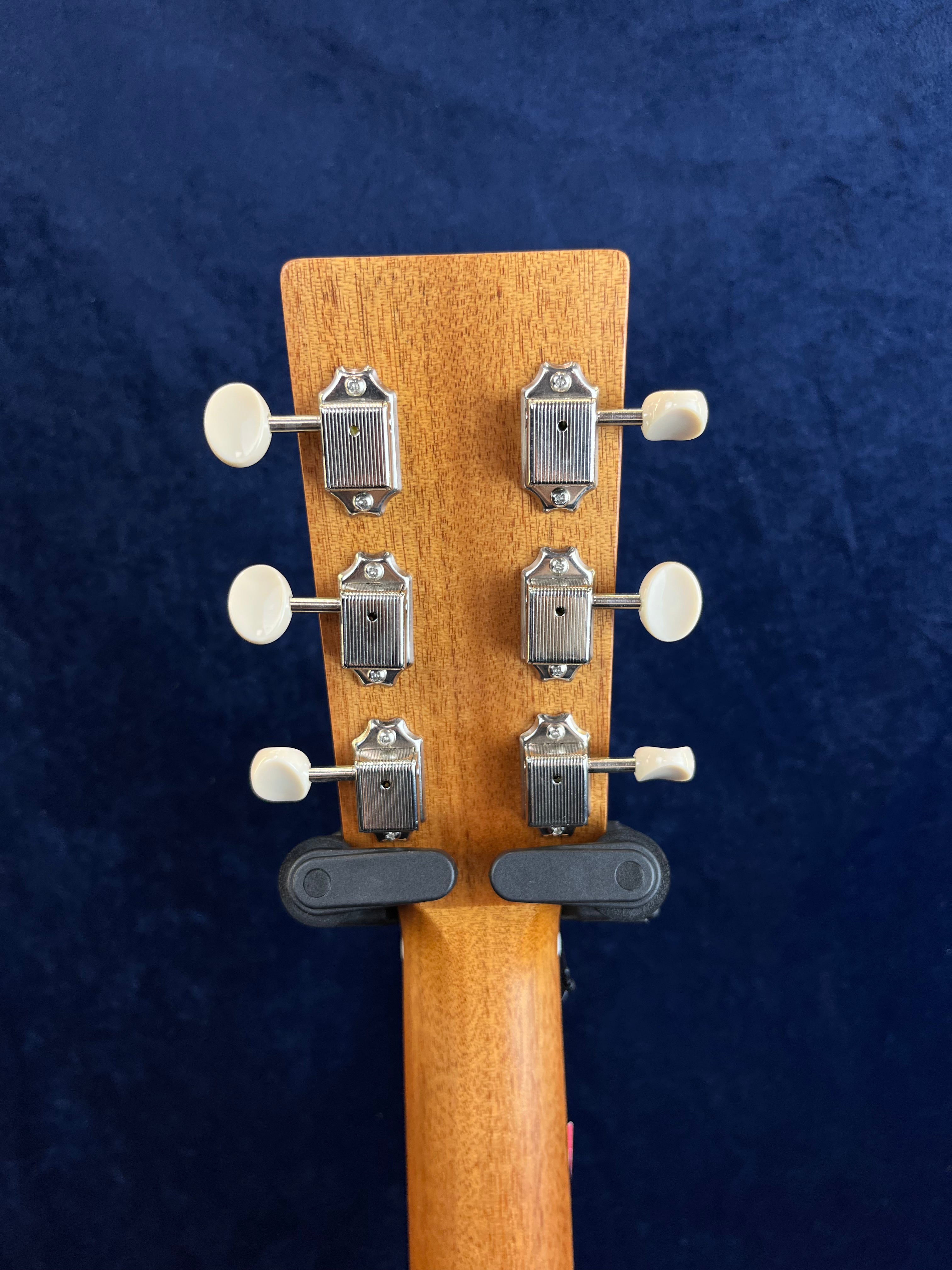 Six mécaniques argentées à boutons blancs sur la tête en bois clair d'une guitare acoustique, fond bleu uni.