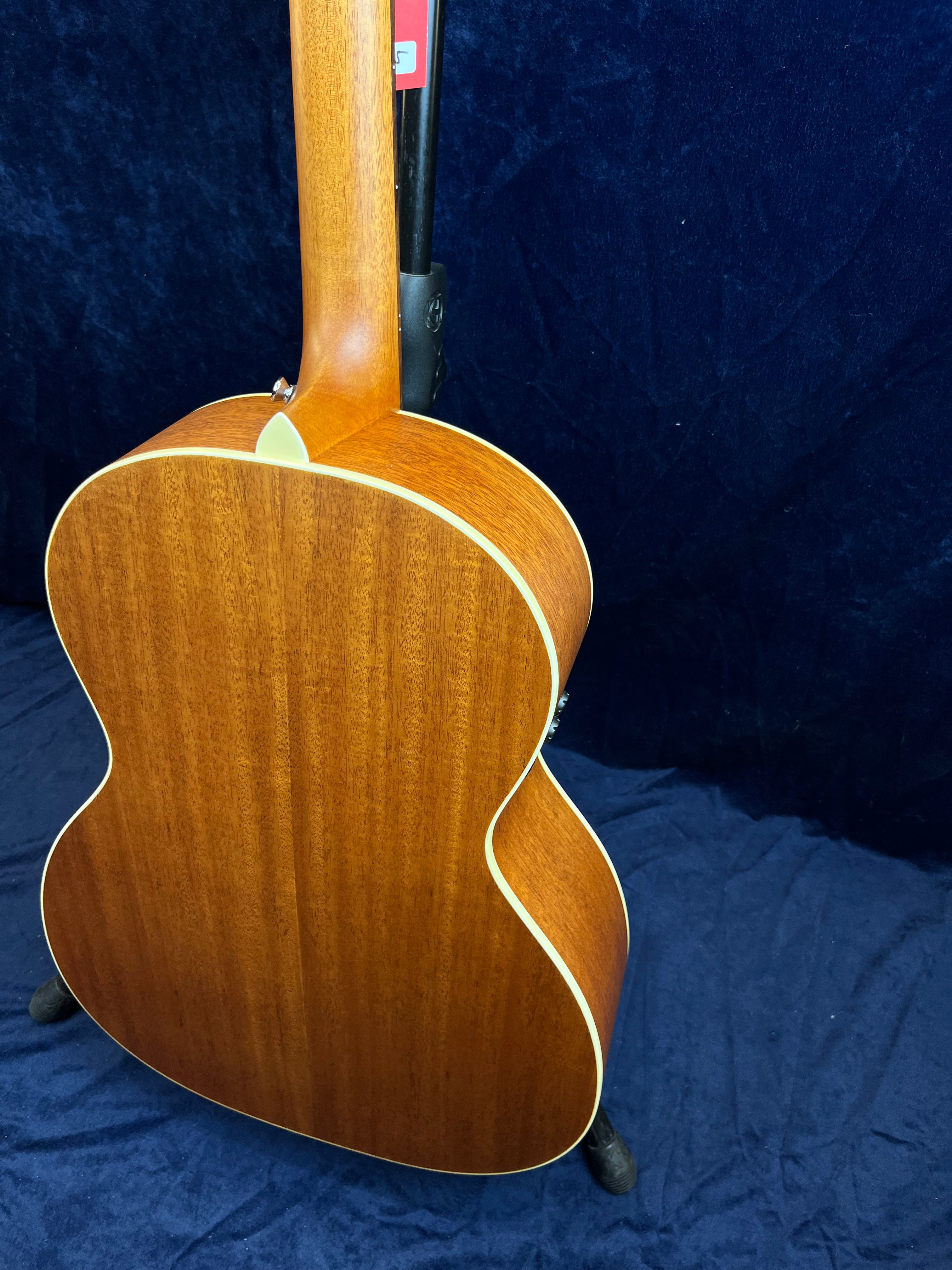 Guitare acoustique avec dos et manche en bois brun mat, contours arrondis soulignés par un filet crème, posée sur un support.