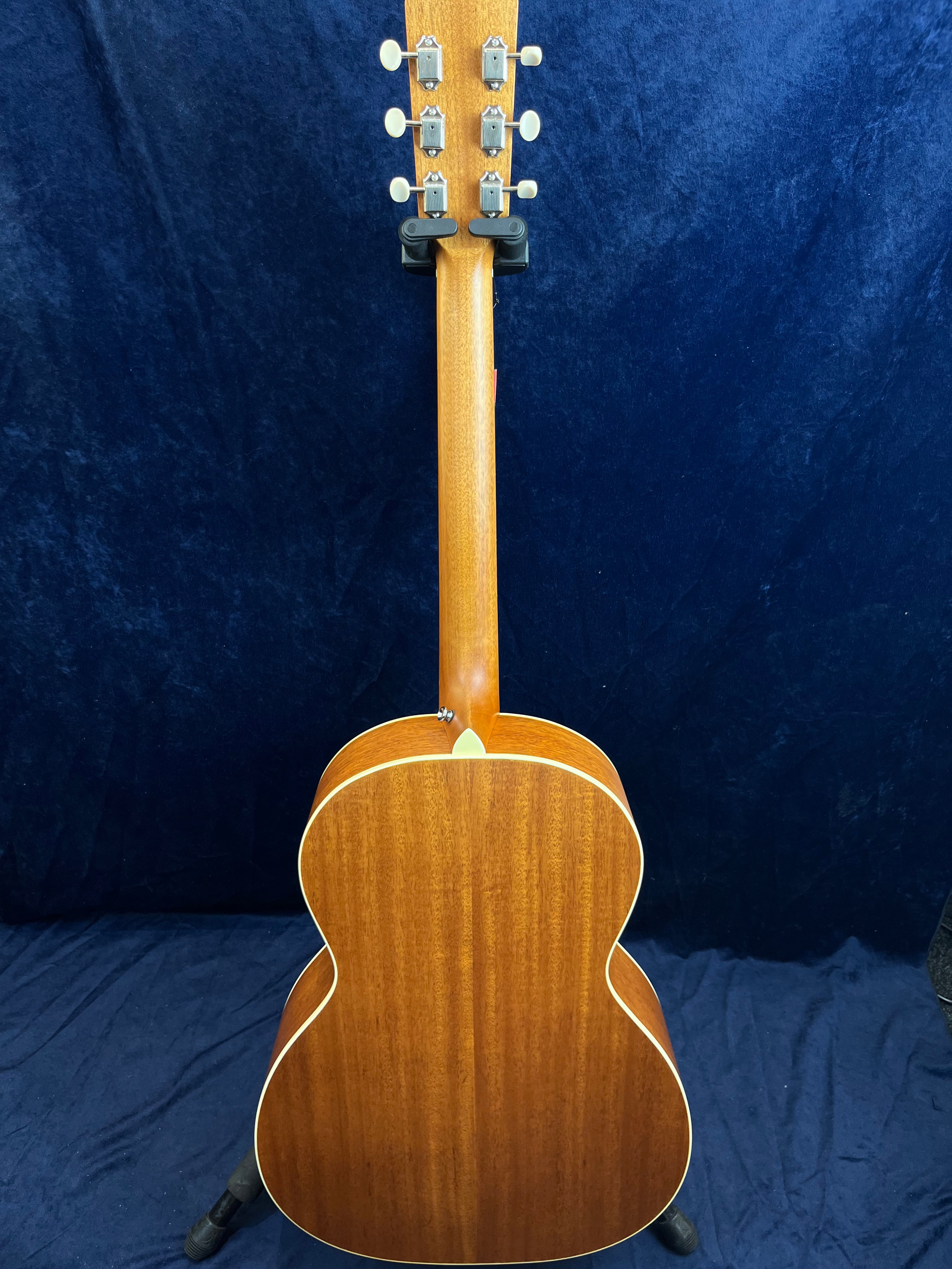 Guitare acoustique en bois vue de dos, finition brun clair, six mécaniques argentées et touches blanches sur la tête, contours clairs.
