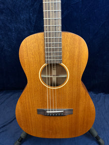Small-bodied acoustic guitar with a natural wood finish, six steel strings, a simple round sound hole, and a dark wood bridge and fretboard.