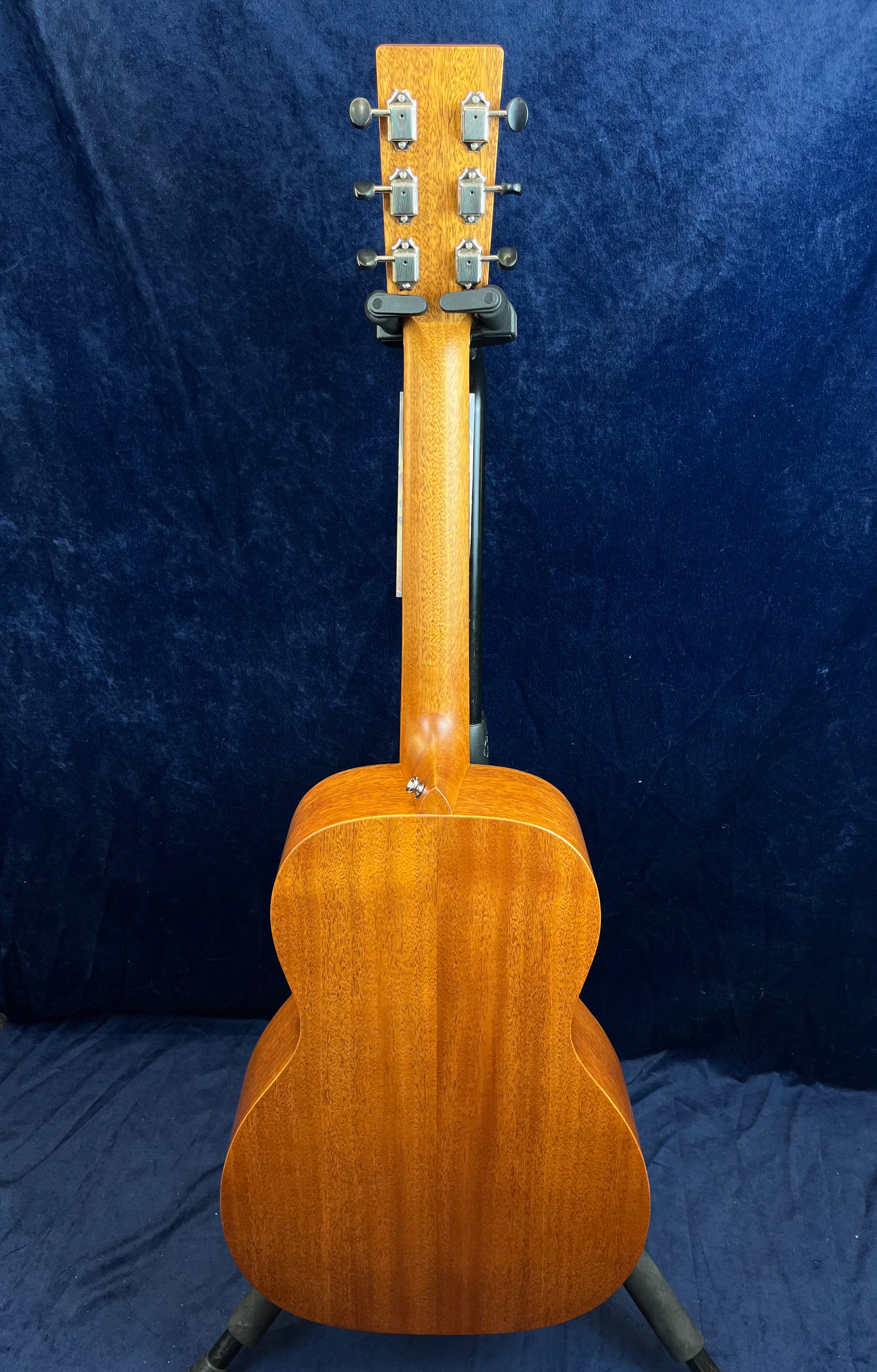Acoustic guitar shown from the back, displaying a smooth, glossy wood finish with six silver tuning pegs on the headstock.