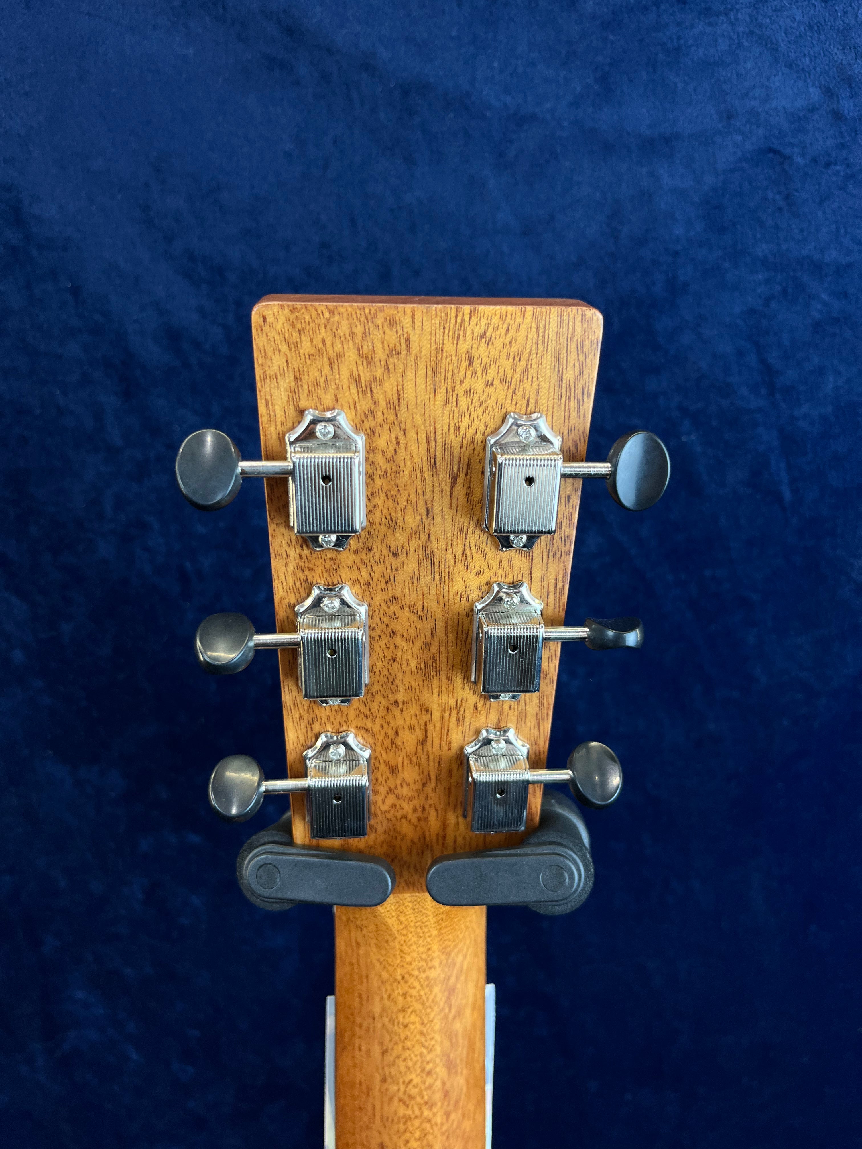 Six silver tuning pegs on a wooden acoustic guitar headstock, viewed from the back against a dark blue background.