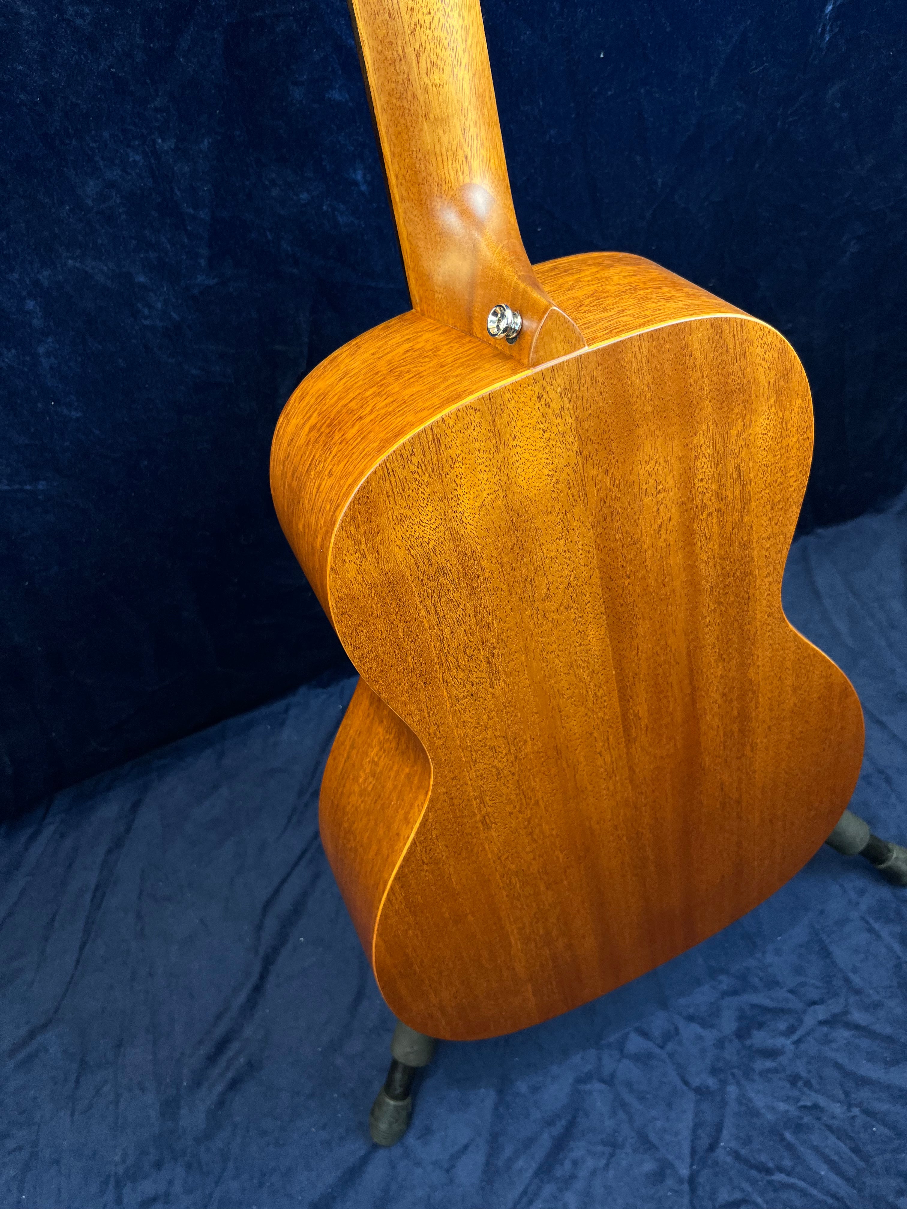 Back view of an acoustic guitar with a natural wood finish, showing its neck joint and side curves against a dark background.