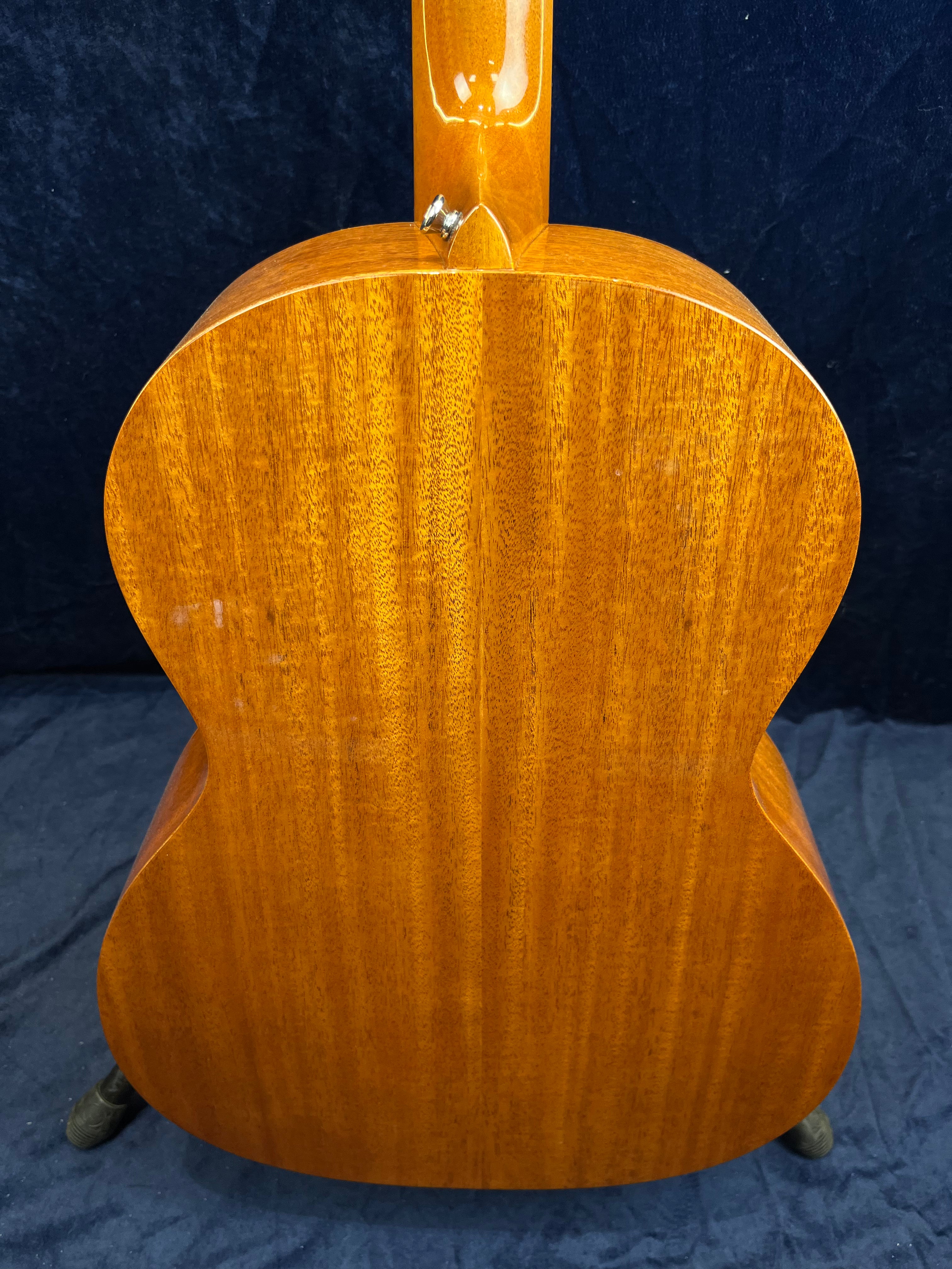 Fond d'une guitare acoustique en bois verni couleur miel, avec des veines verticales fines et un attache-courroie métallique à la base du manche.