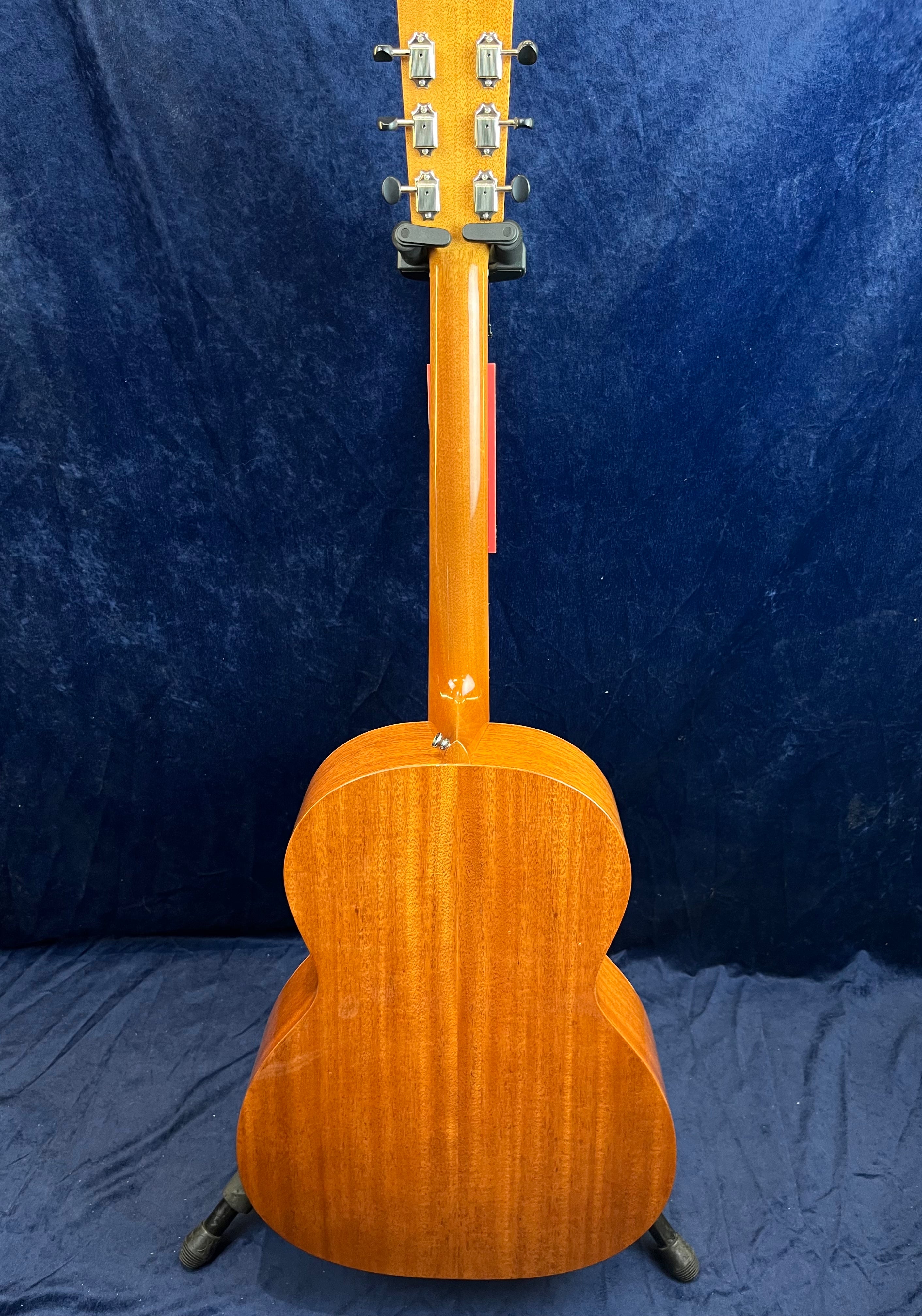 Guitare acoustique en bois clair vue de dos, montrant le manche et le dos bombé avec un veinage vertical, posée sur un support.