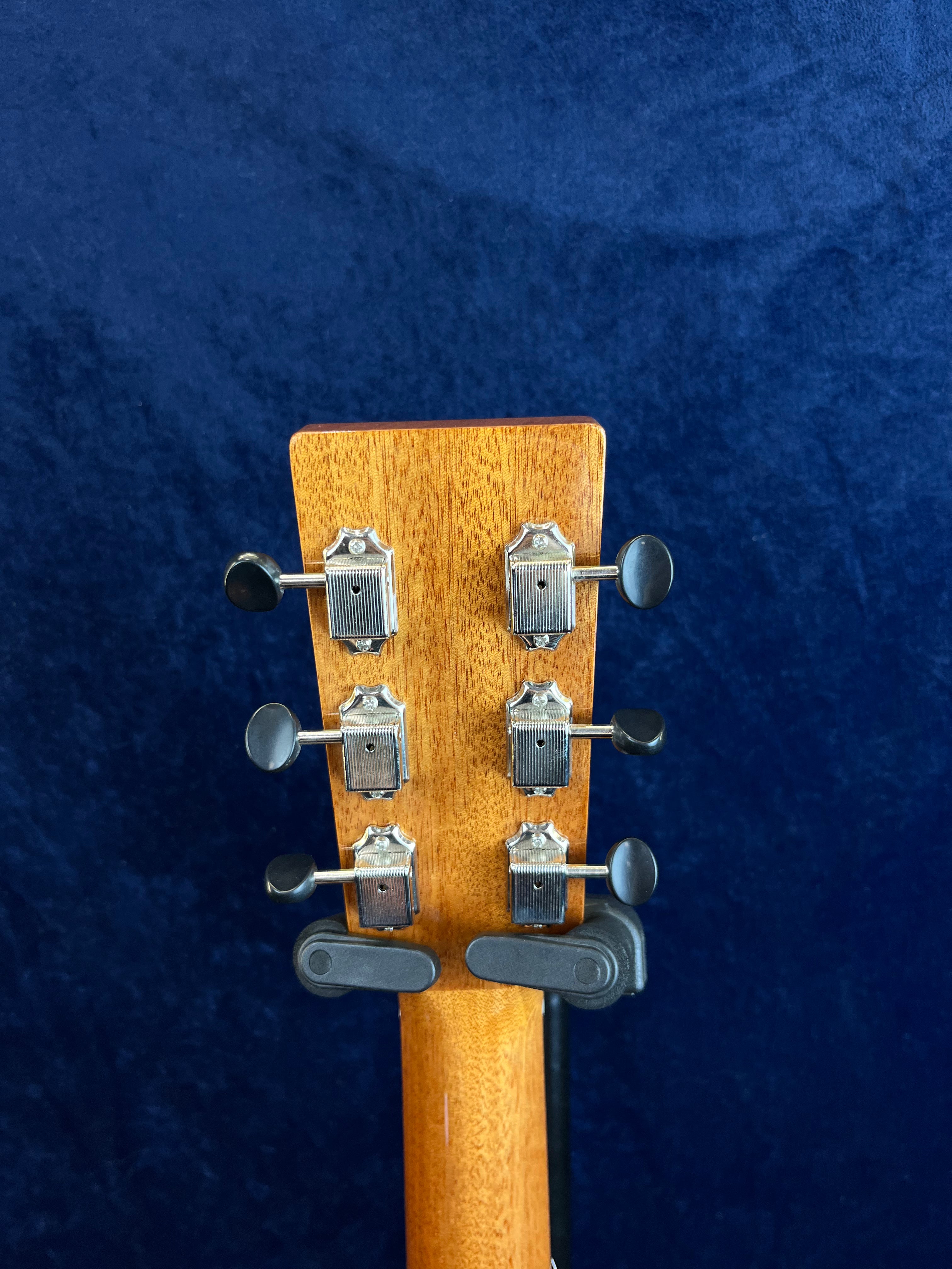 Six silver tuning pegs with black knobs on the back of a wooden acoustic guitar headstock, set against a dark blue textured background.