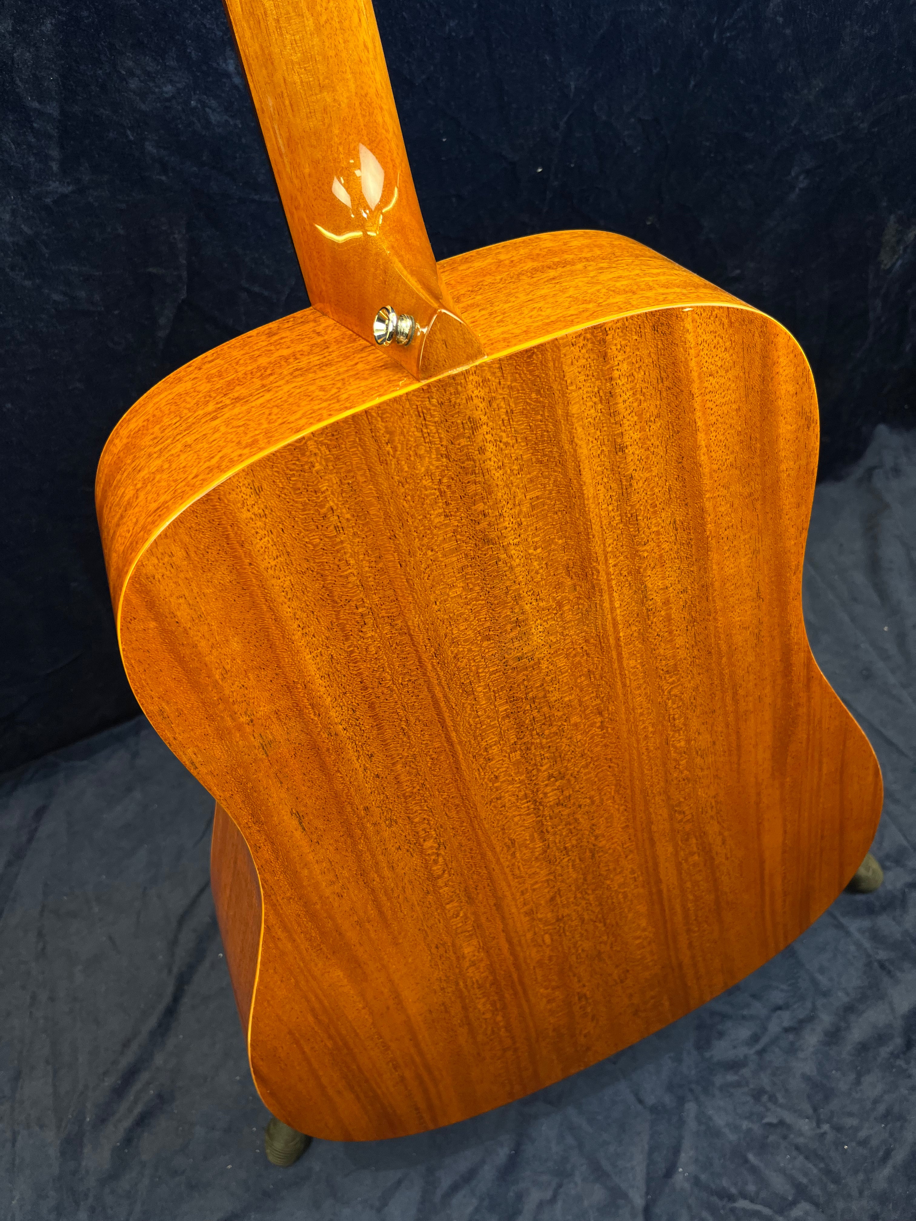 Rich brown acoustic guitar back and neck with visible wood grain, no visible hardware, body has a natural glossy finish and a strap button on the heel.