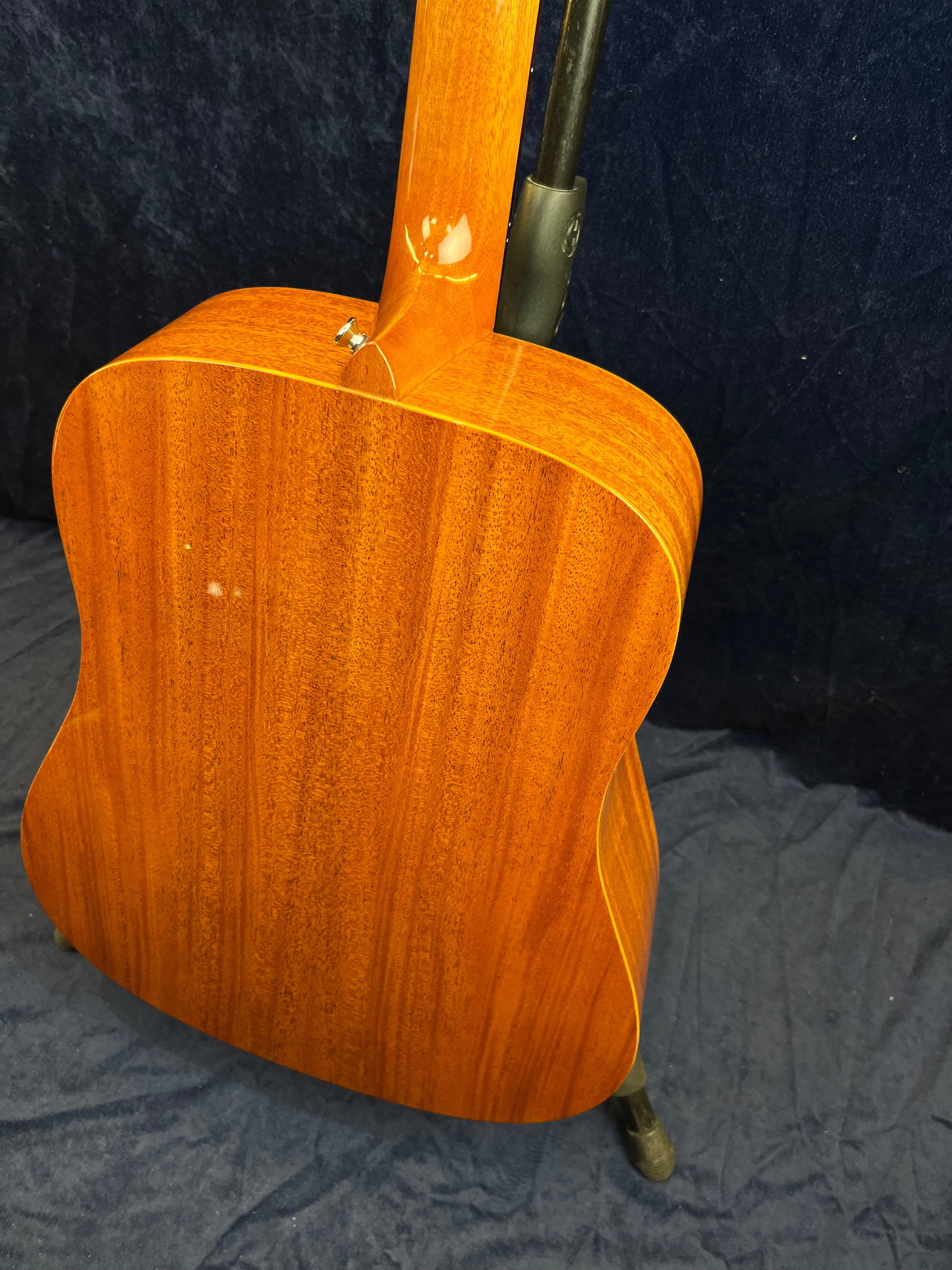 Back and neck of a brown acoustic guitar with a glossy wood finish, showing subtle vertical grain patterns and a small spot on the back.