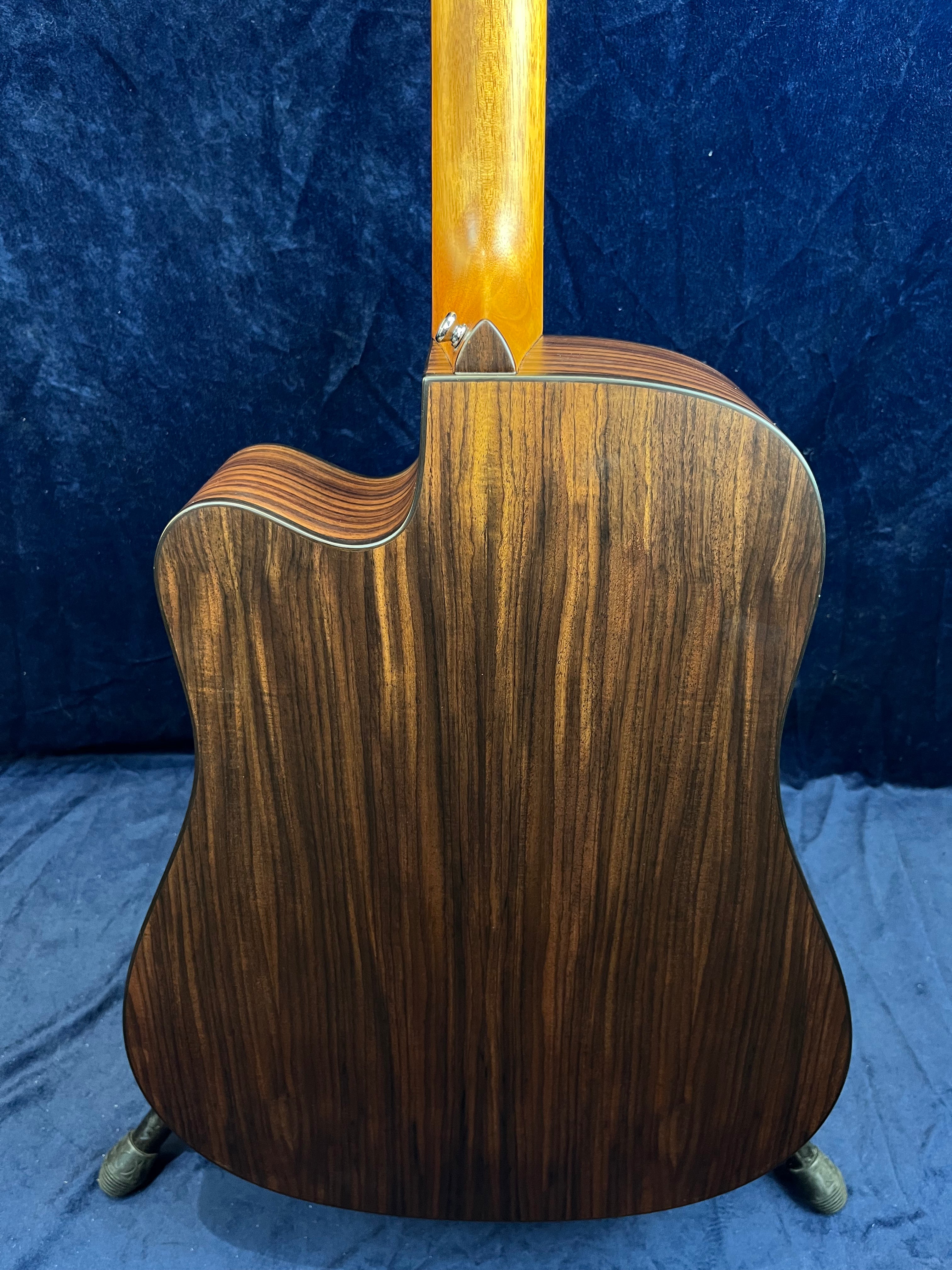 Guitare acoustique avec dos en bois foncé veinuré, manche en bois clair, pan coupé à gauche, posée sur une housse bleue.
