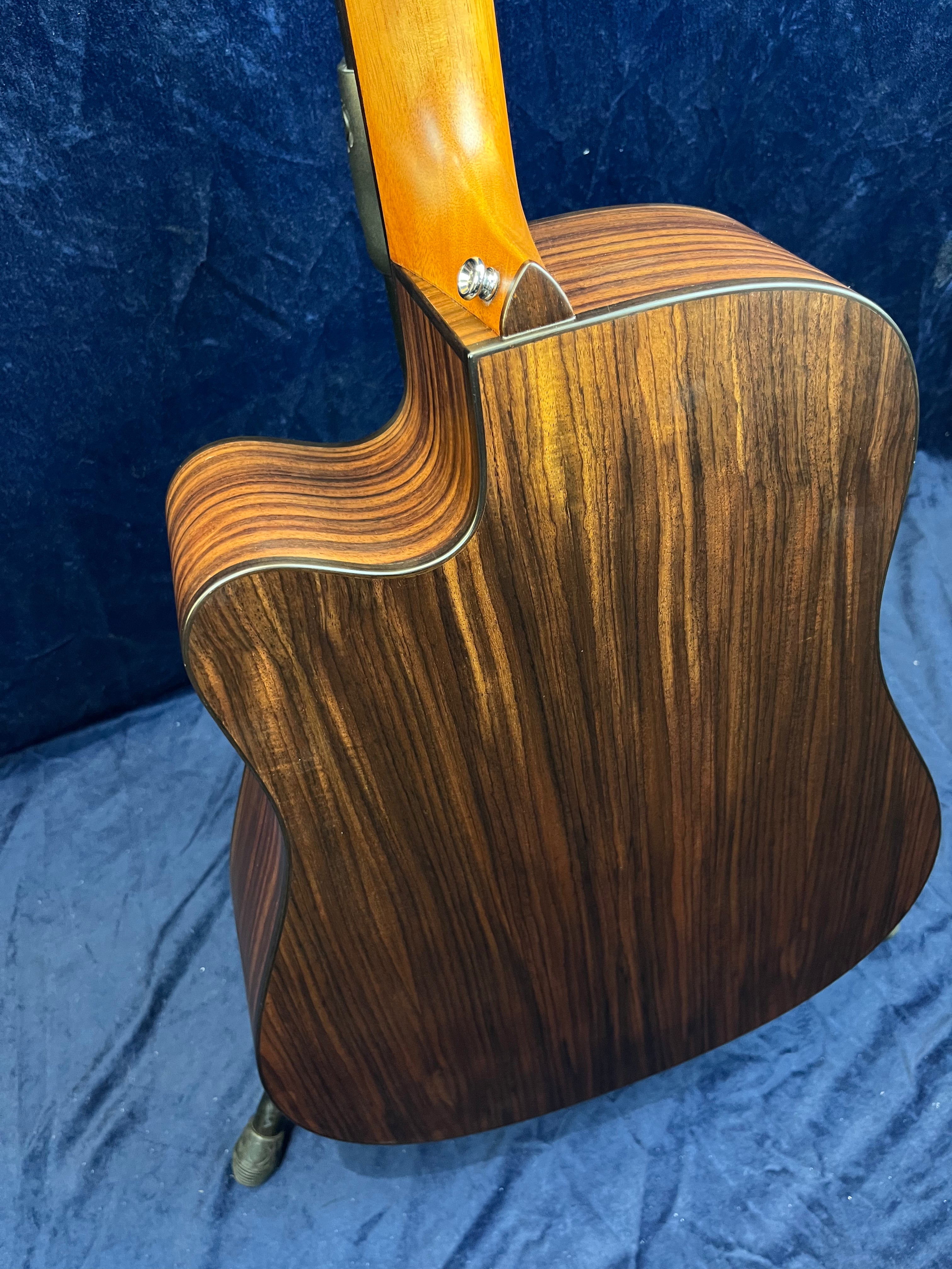 Guitare acoustique avec dos en bois foncé à veines claires, éclisse incurvée et manche collé teinté miel mat.
