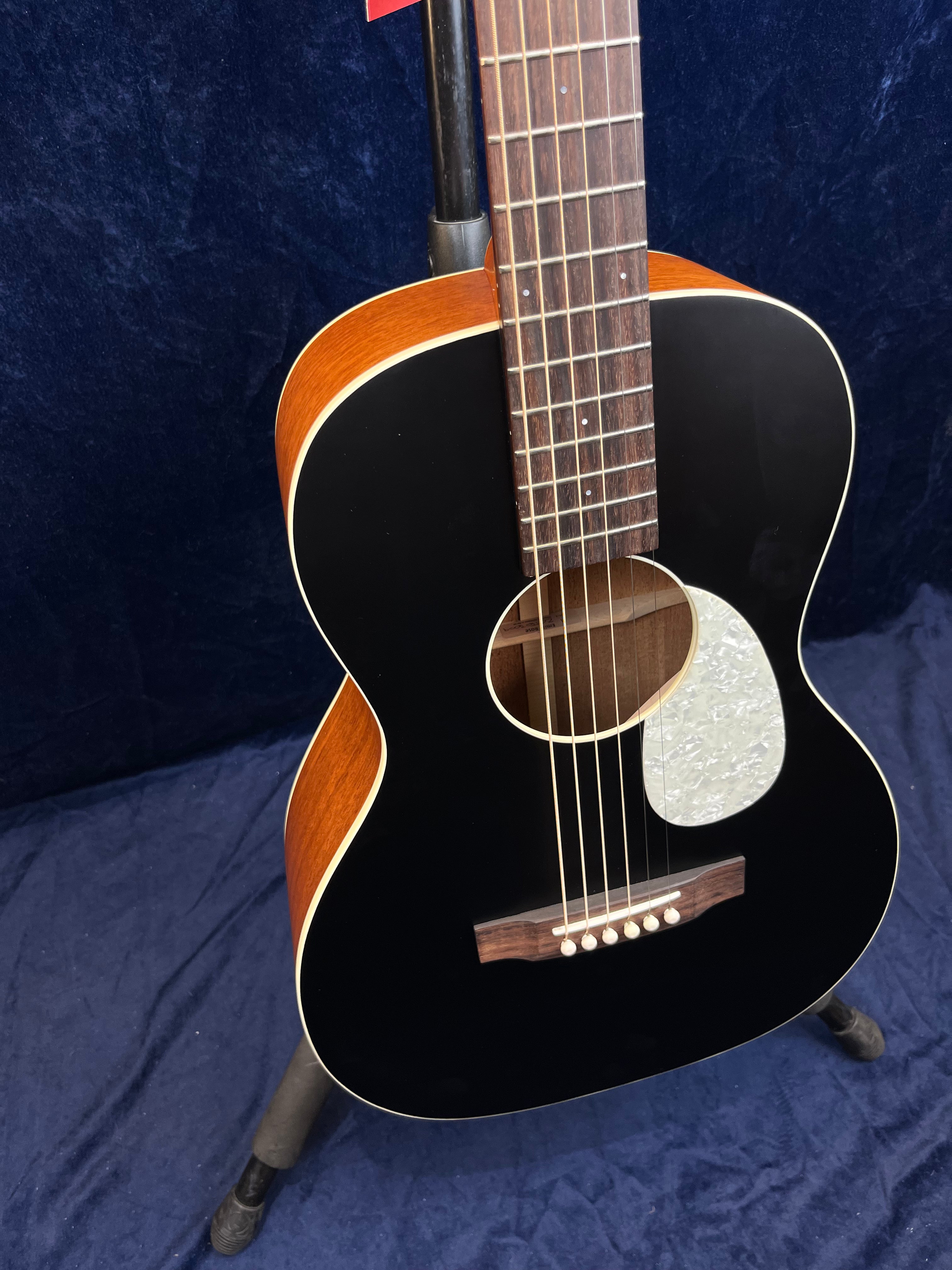 Acoustic guitar with a black front, pearl white pickguard, natural wood sides, six strings, and a dark wood fingerboard on a stand.