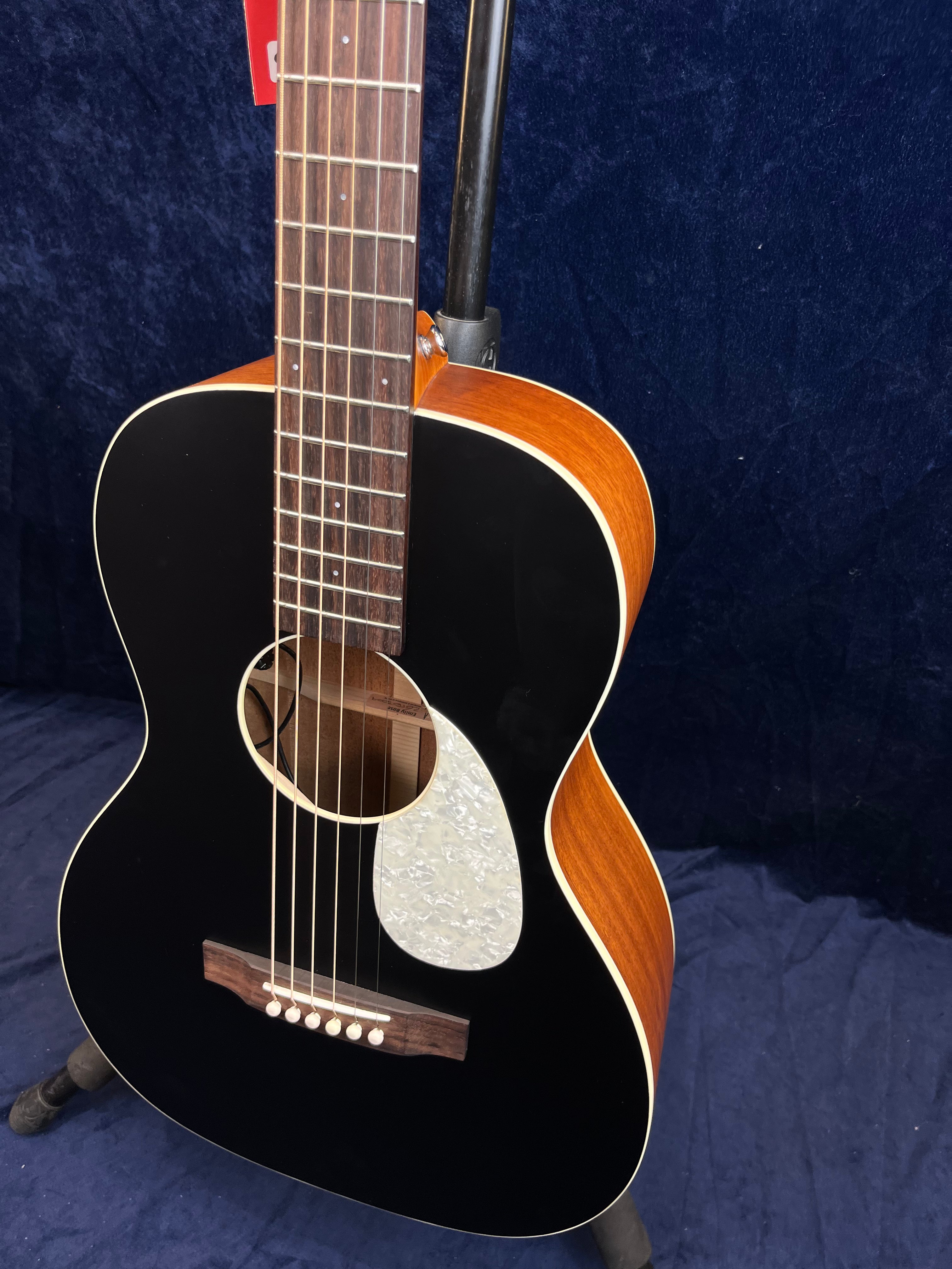 Acoustic guitar with a black front, white pearloid pickguard, six strings, wooden bridge, and brown sides and neck against a dark blue background.