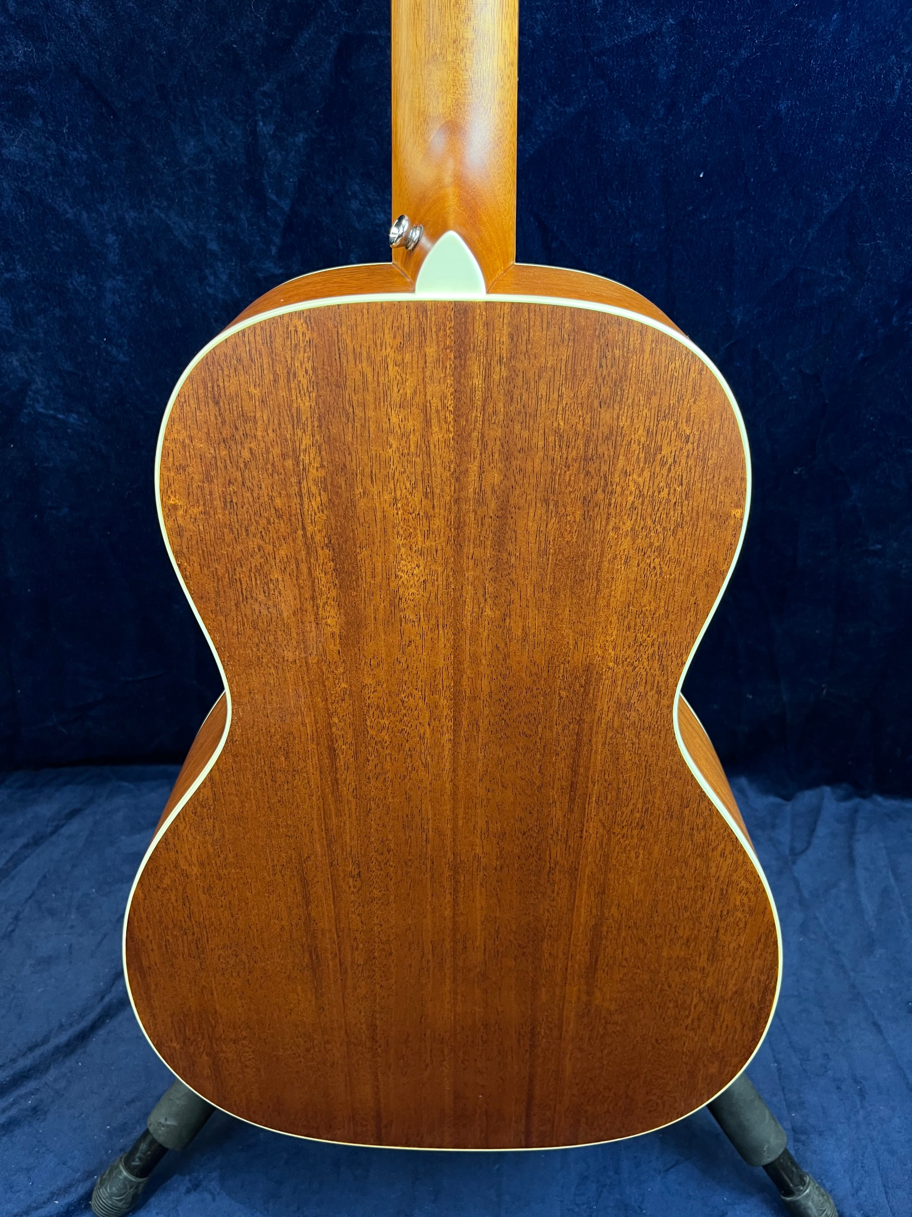 Back view of an acoustic guitar showing smooth, reddish-brown wood with light cream binding along the edges, set against a dark background.