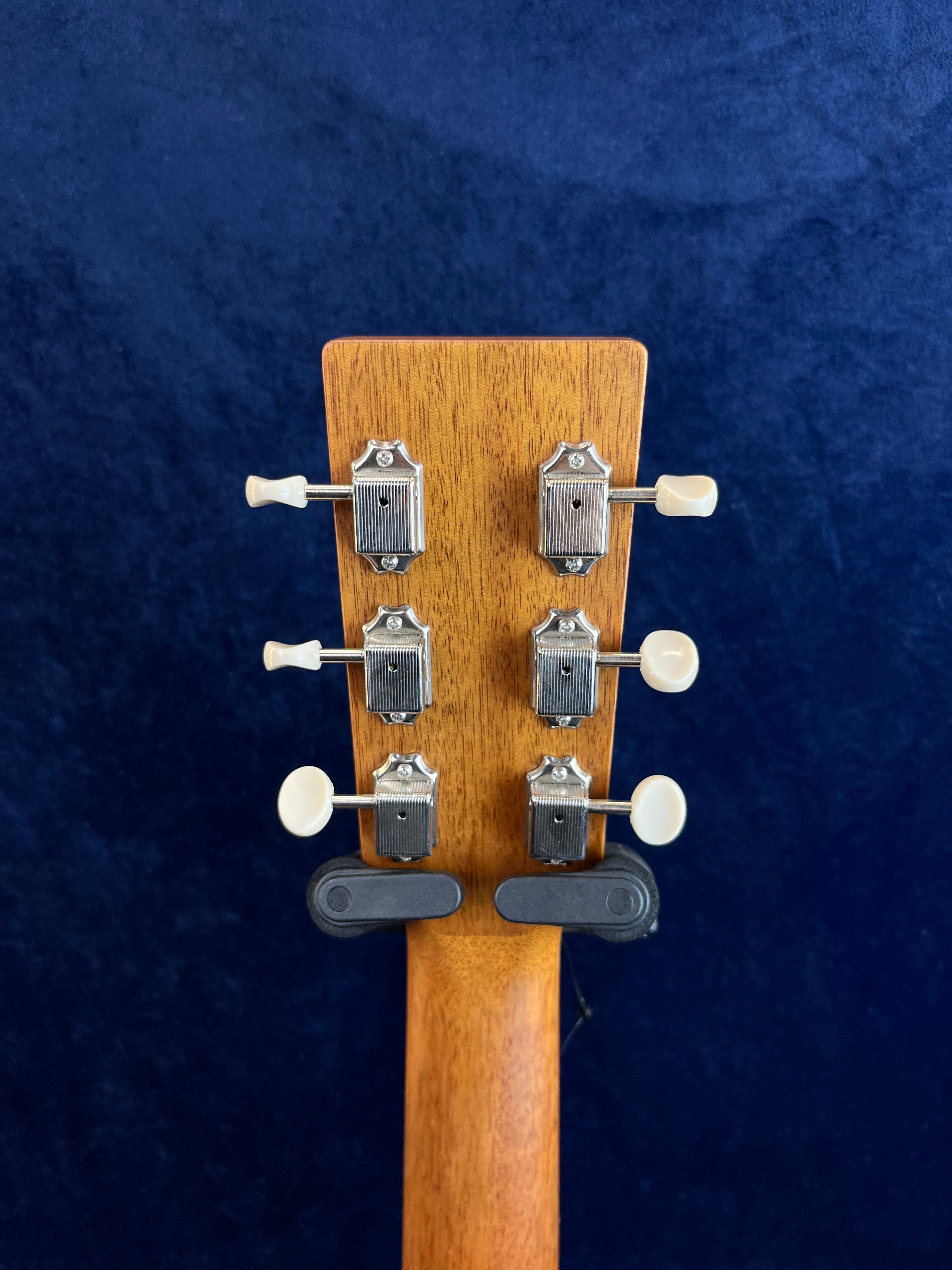 Back of an acoustic guitar headstock, showing six silver tuning pegs with white knobs against a dark blue background.