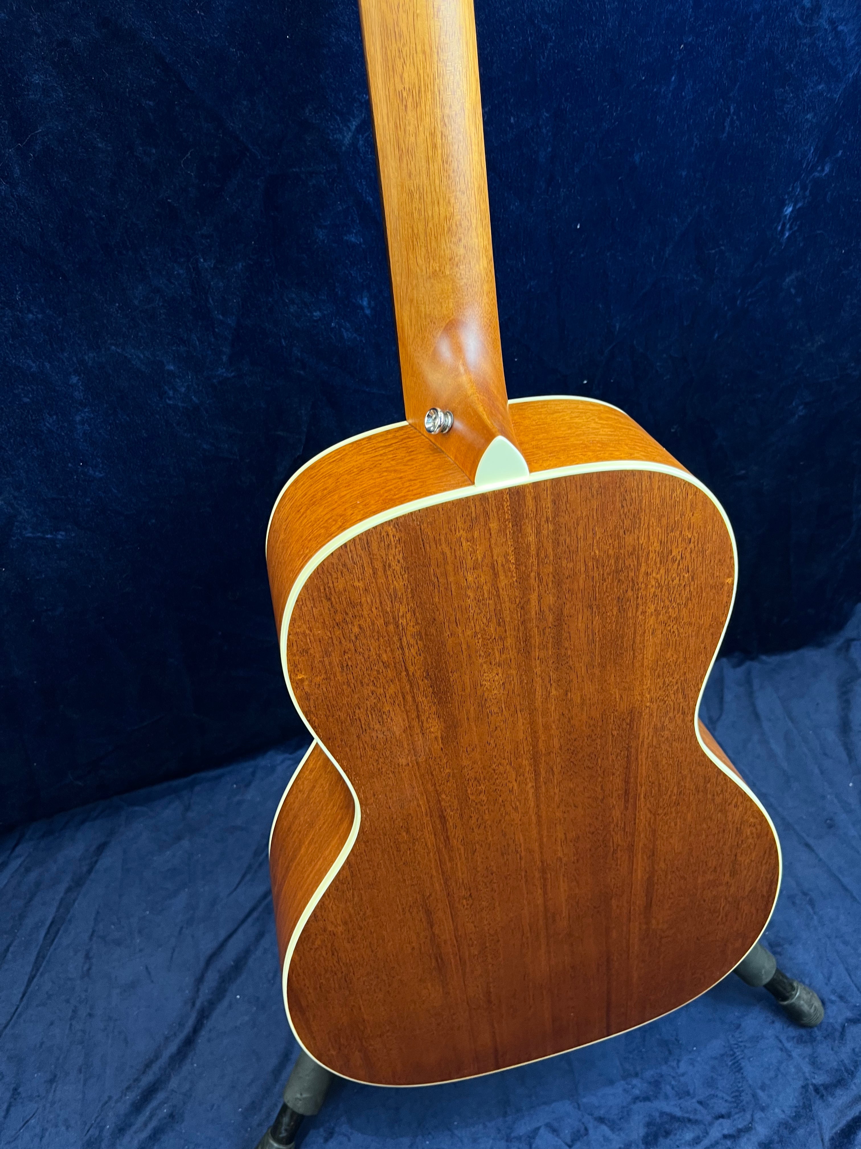 Acoustic guitar shown from the back, featuring a smooth, light brown wood finish with cream-colored edge binding and a strap button near the neck joint.