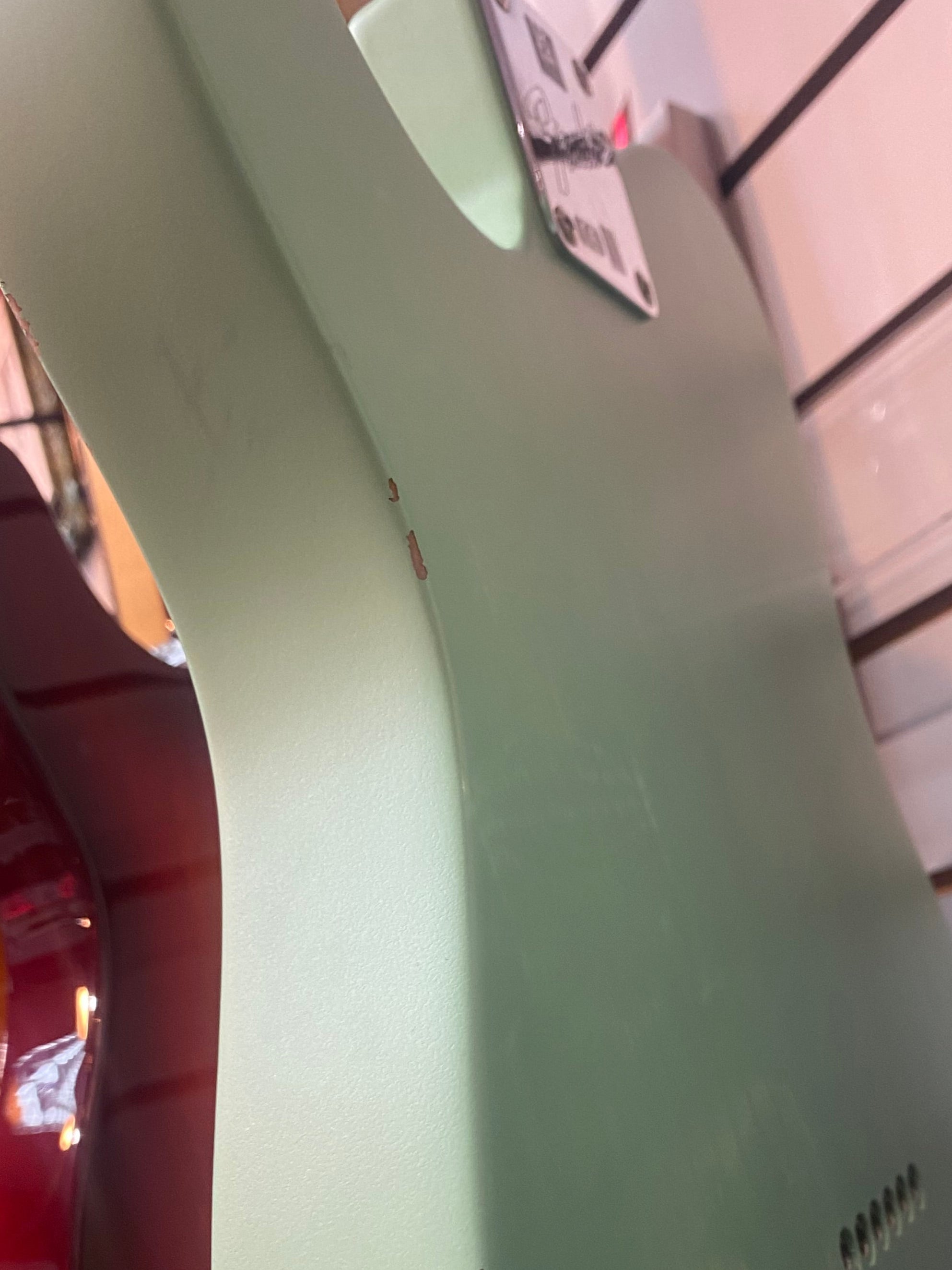 Light green electric guitar body with visible chipped paint along the edge, photographed from the back at an angle.