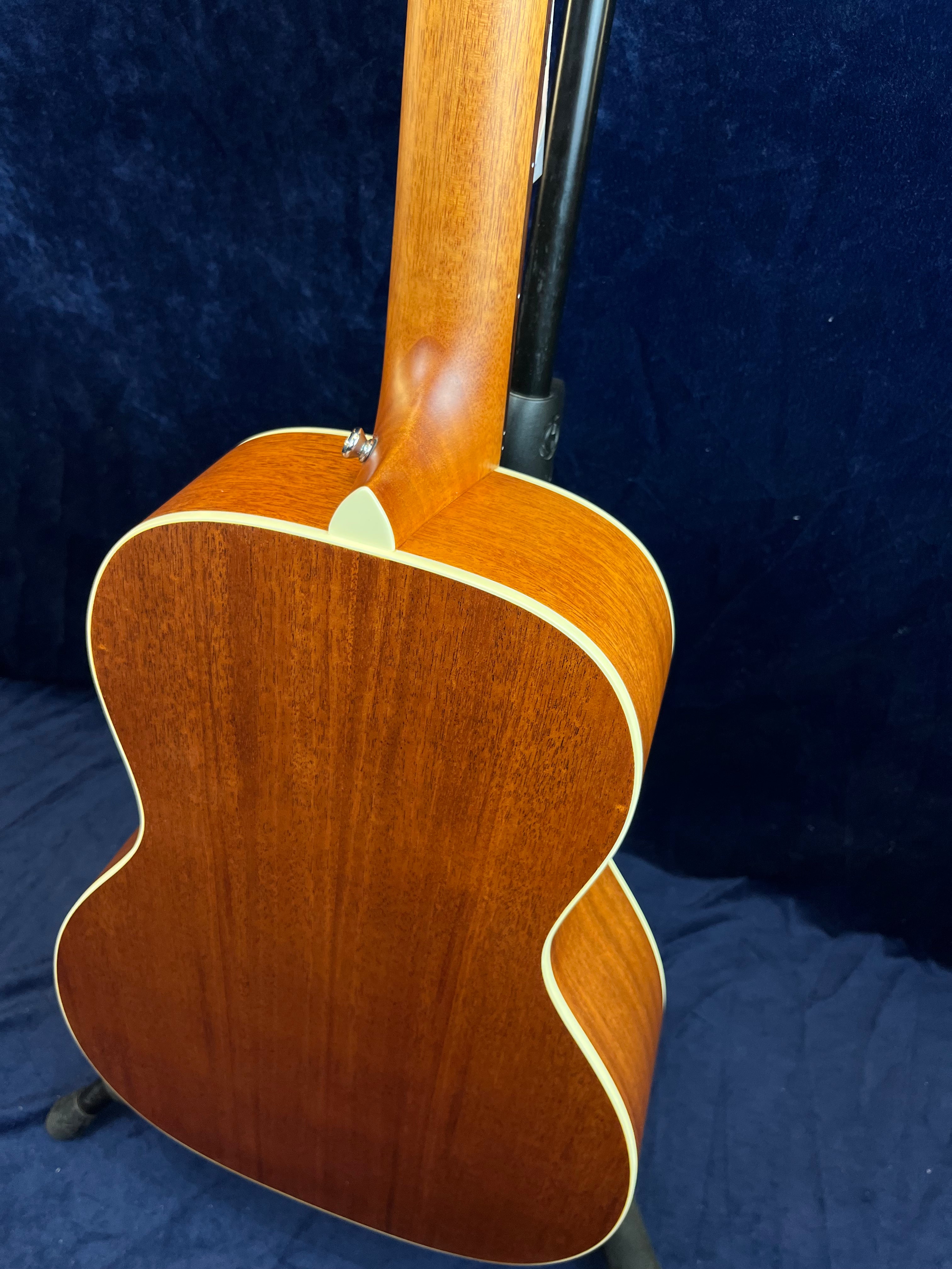 Acoustic guitar with a smooth, natural wood back and cream binding along the edges, shown on a stand against a dark blue background.