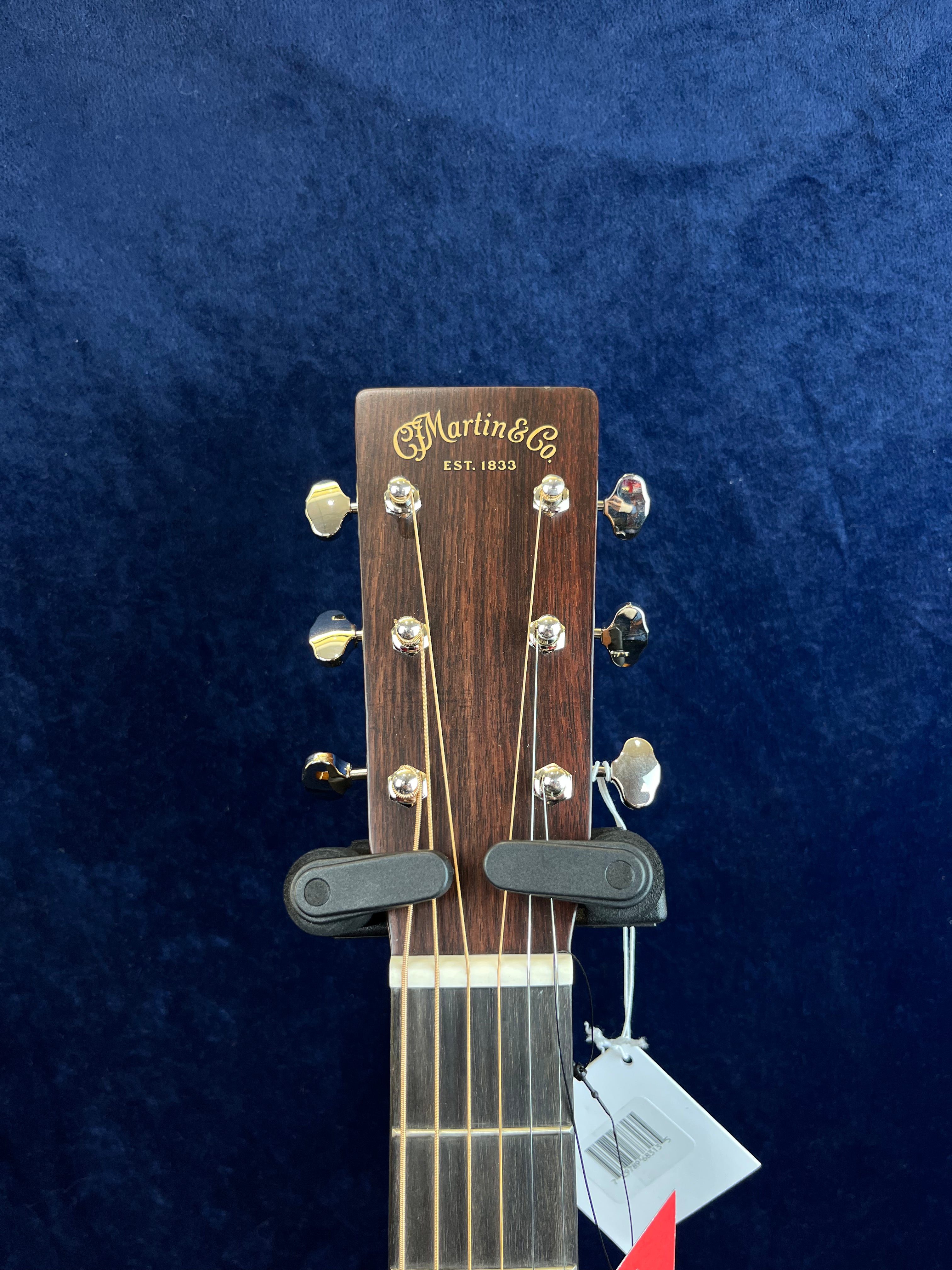 C.F. Martin & Co. acoustic guitar headstock with six tuning pegs, gold logo, and two black hangers holding the neck against a dark blue background.