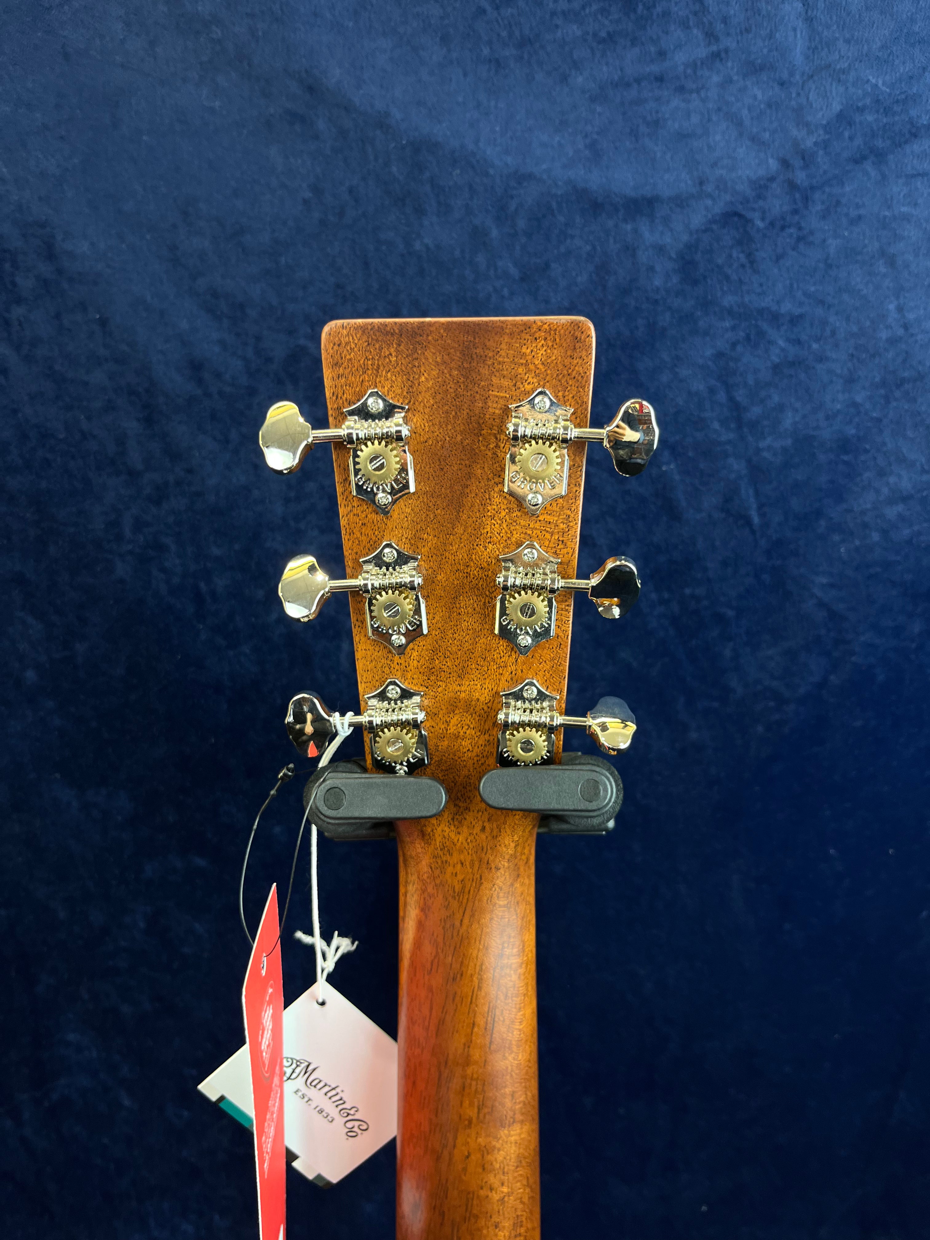 Back of an acoustic guitar headstock showing six vintage-style metal tuning gears, wooden finish, and hanging tags with Martin & Co branding.